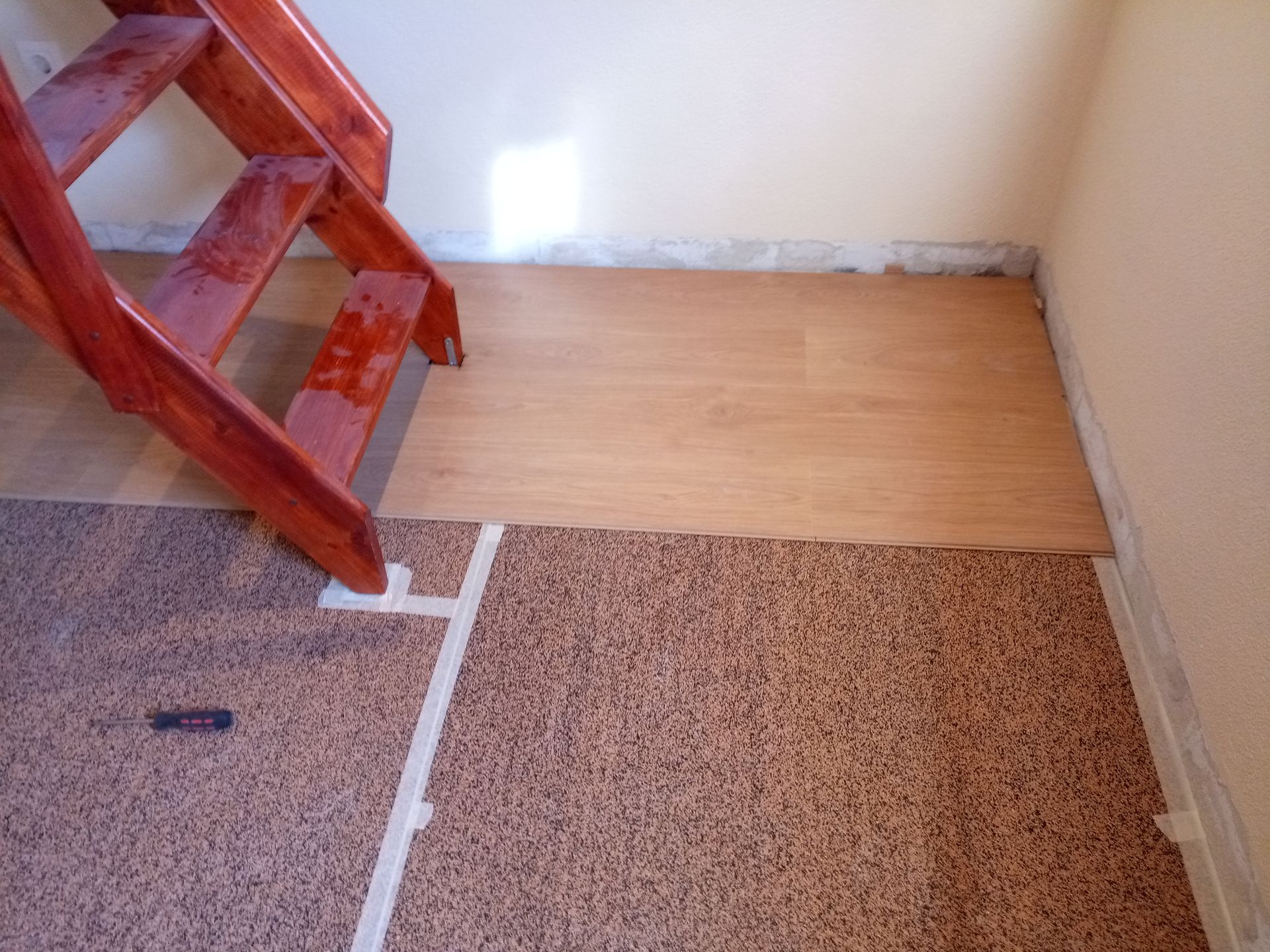 Escada com piso de madeira e carpete, linha de transição demarcada com fita adesiva.