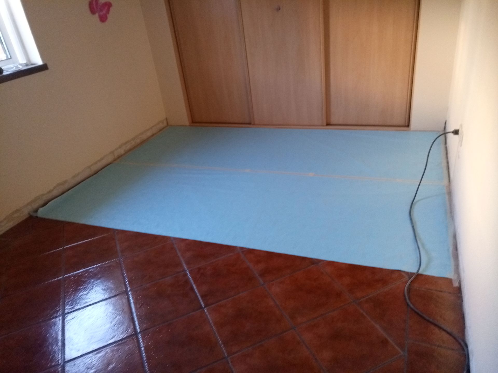 Quarto com piso de azulejo marrom e espuma azul cobrindo parte dele, com portas de armário ao fundo.