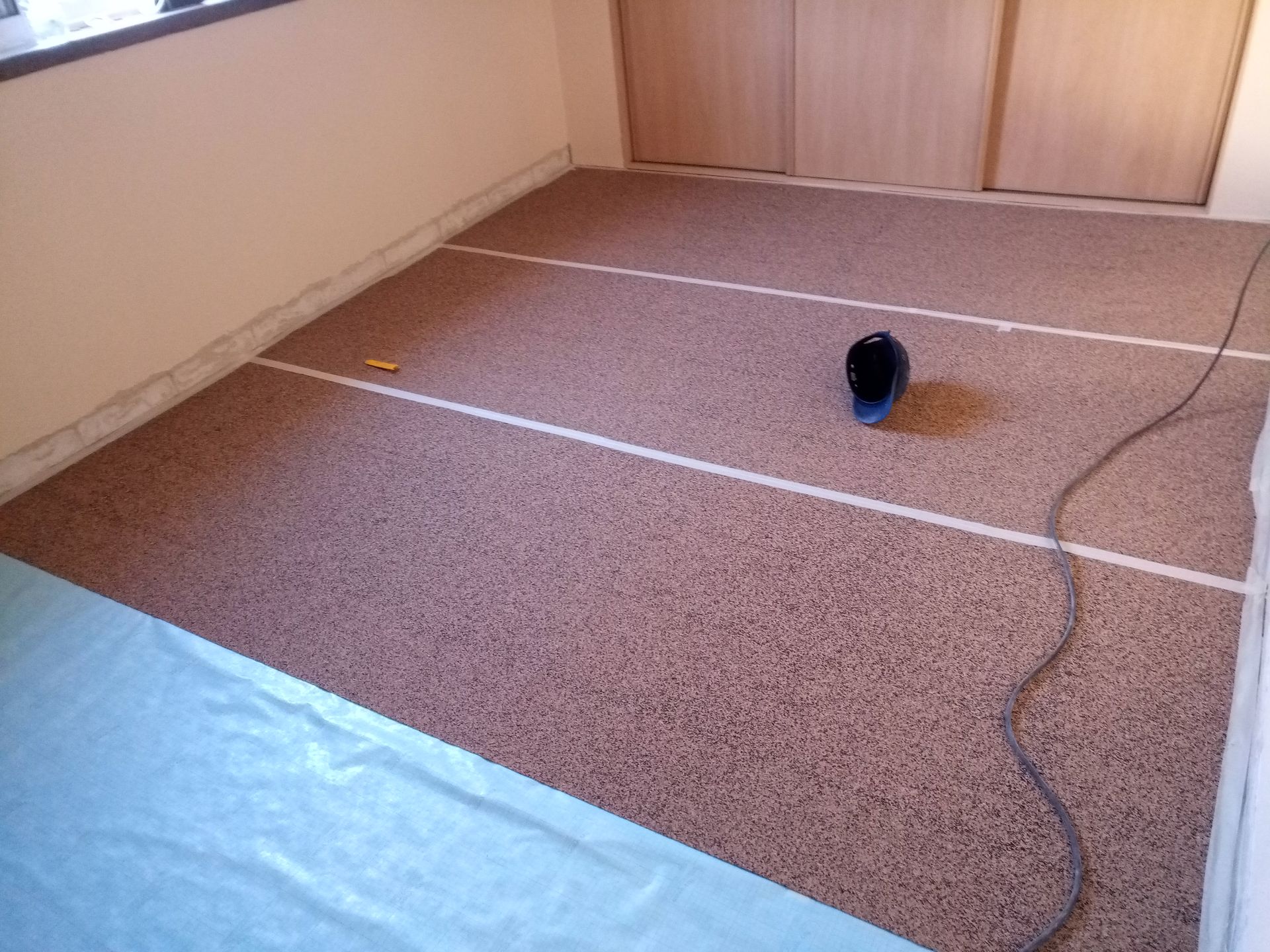 Piso marrom com listras brancas, lona azul, sapato e fio elétrico em um cômodo.