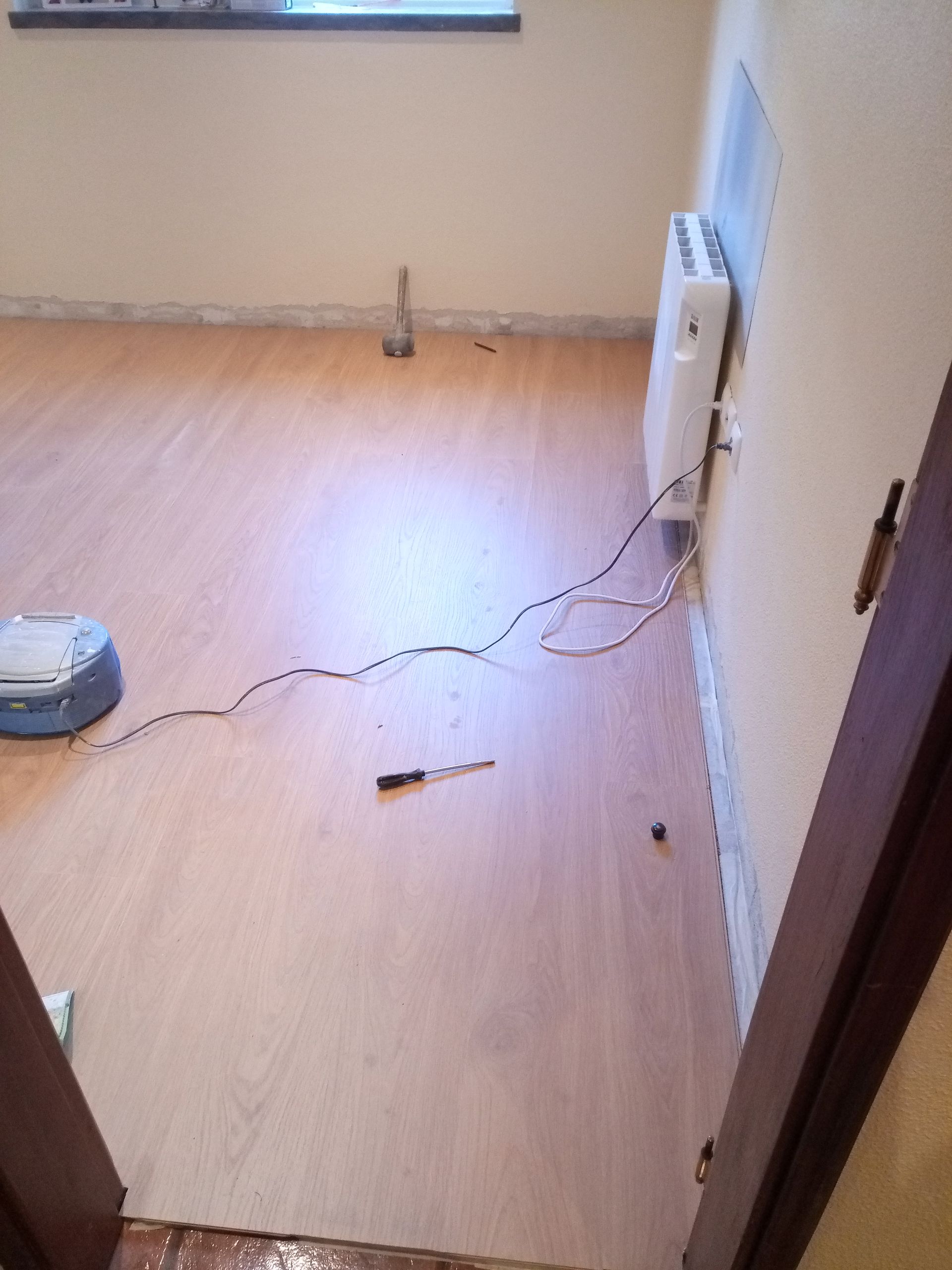 Quarto com piso de madeira, fios elétricos, aquecedor, batente de porta entreaberto e uma caneta.