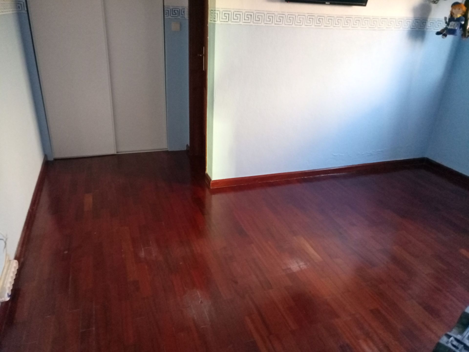 Piso de madeira em um quarto com paredes brancas e azuis, uma moldura de porta e um armário.