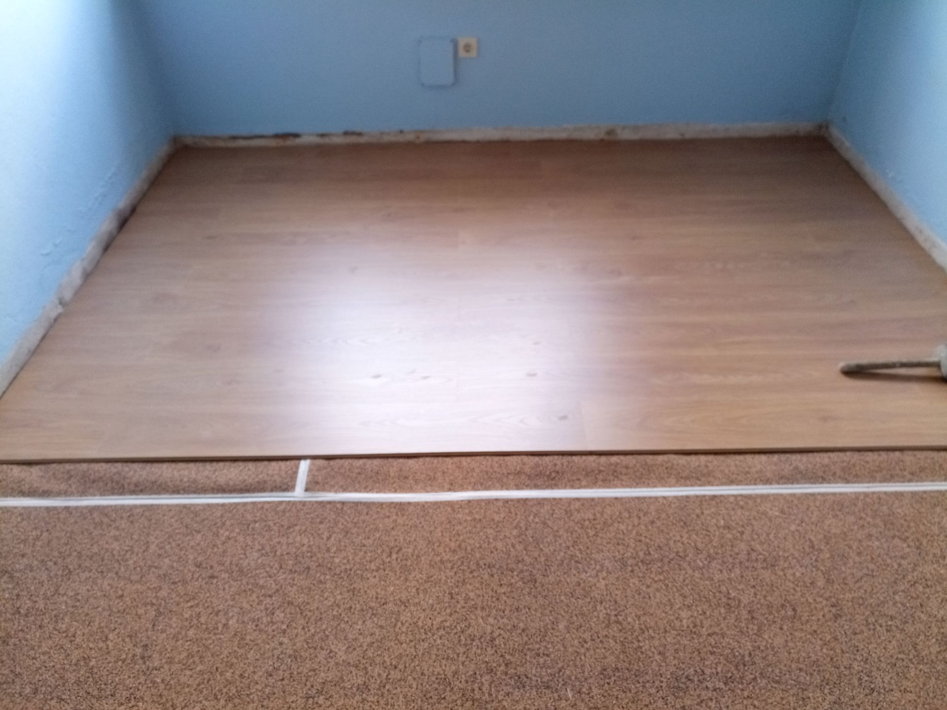 Um quarto com piso laminado bege, carpete marrom e paredes azuis.