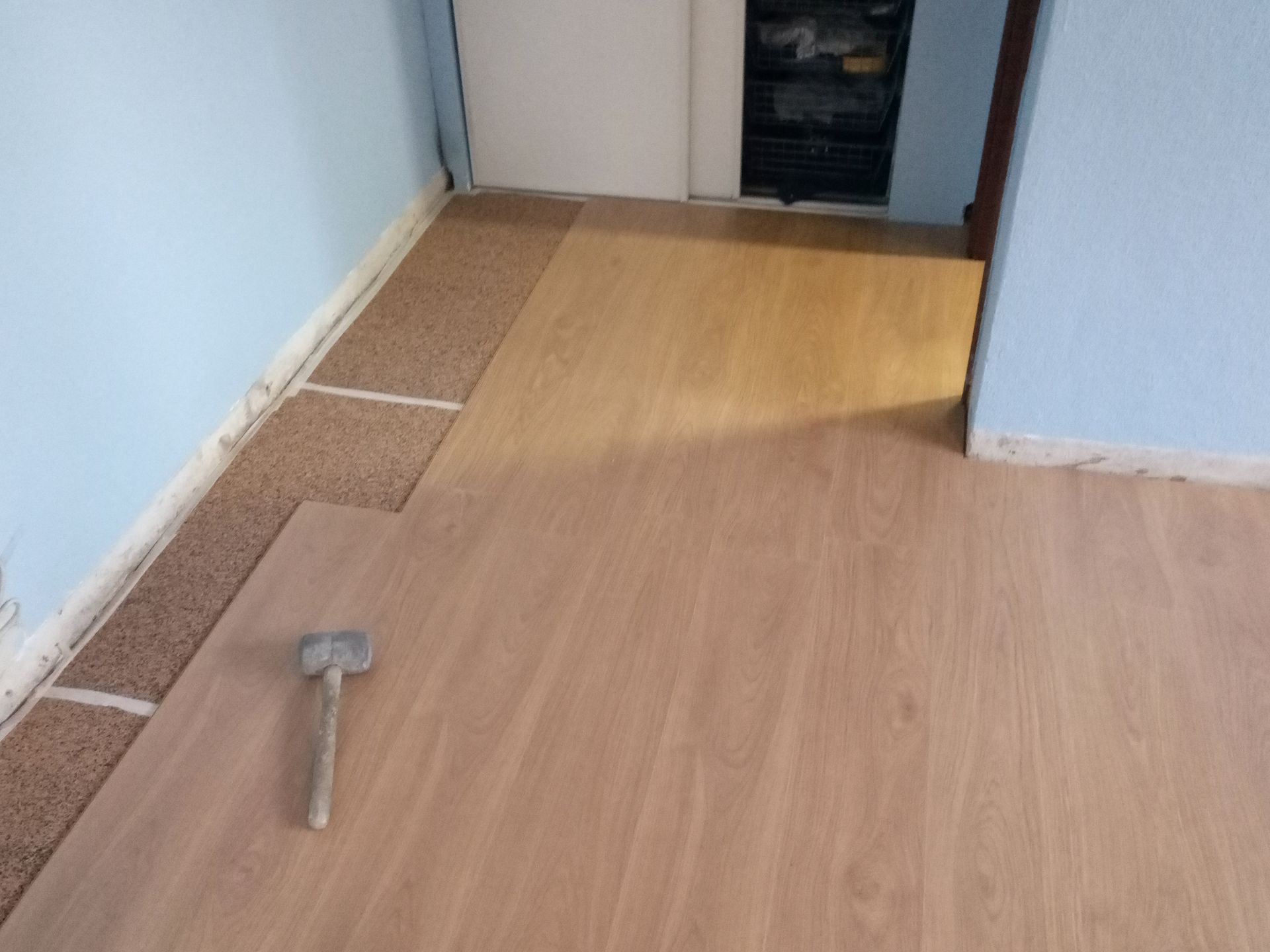 Instalando piso imitando madeira em um cômodo com paredes azuis. Um martelo está sobre uma tábua.