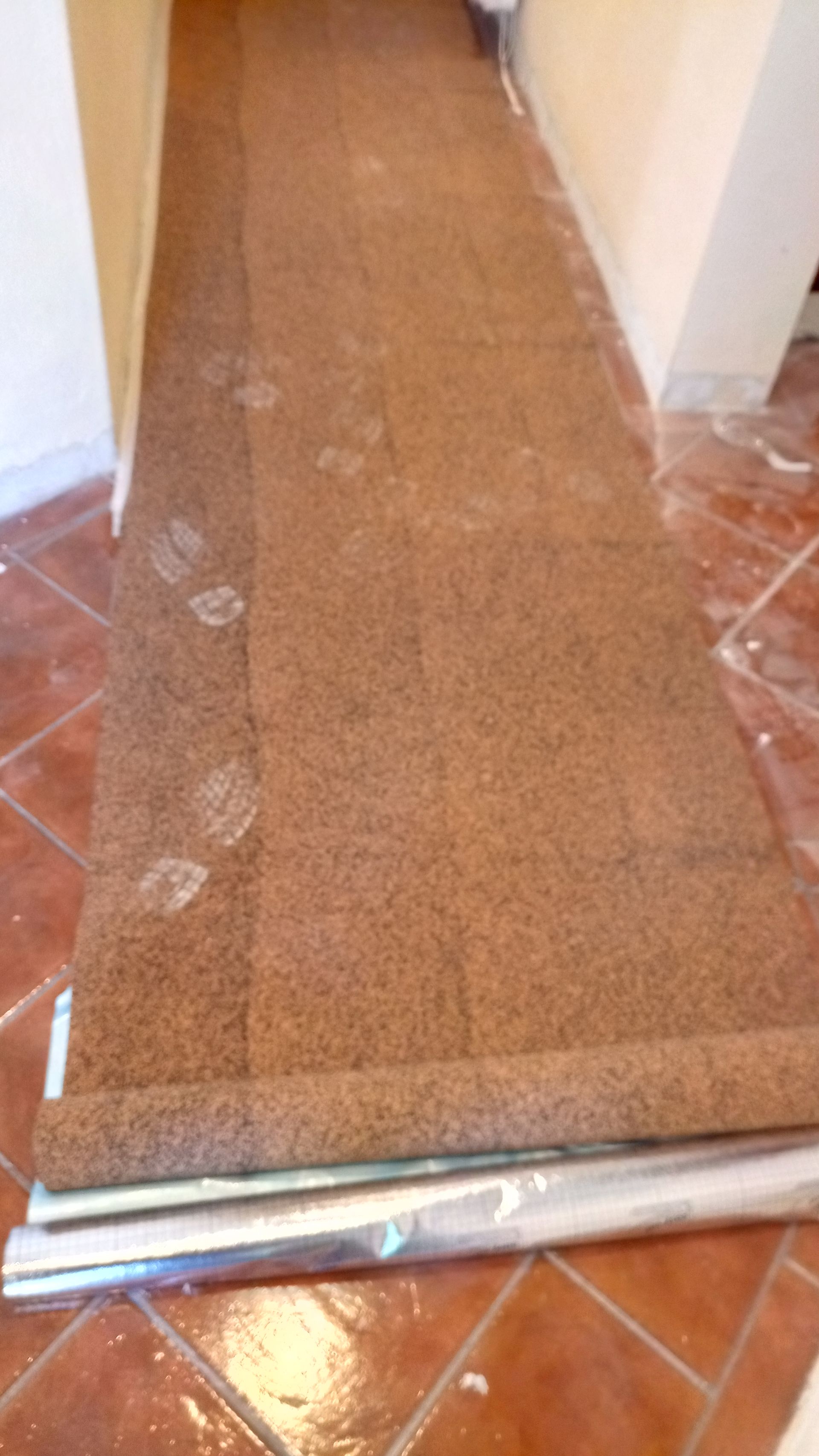 Revestimento protetor de piso marrom instalado em um corredor com ladrilhos cor terracota.