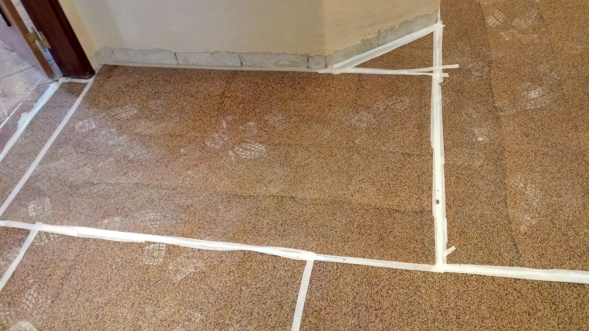 Piso marrom com pintas, rejunte branco e moldura de canto, próximo a uma porta.