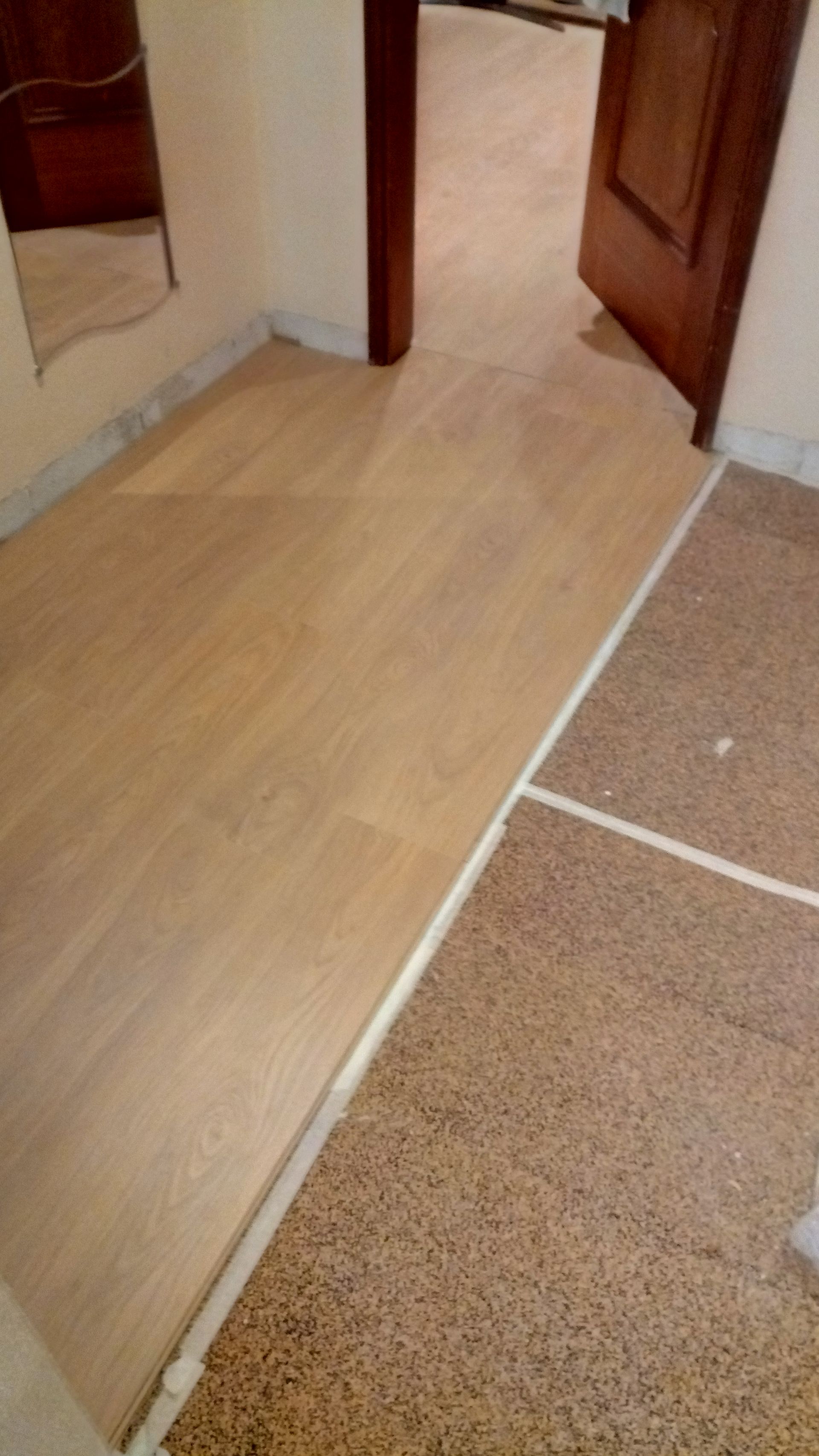 Piso de madeira instalado ao lado do piso de terrazzo existente em uma entrada.