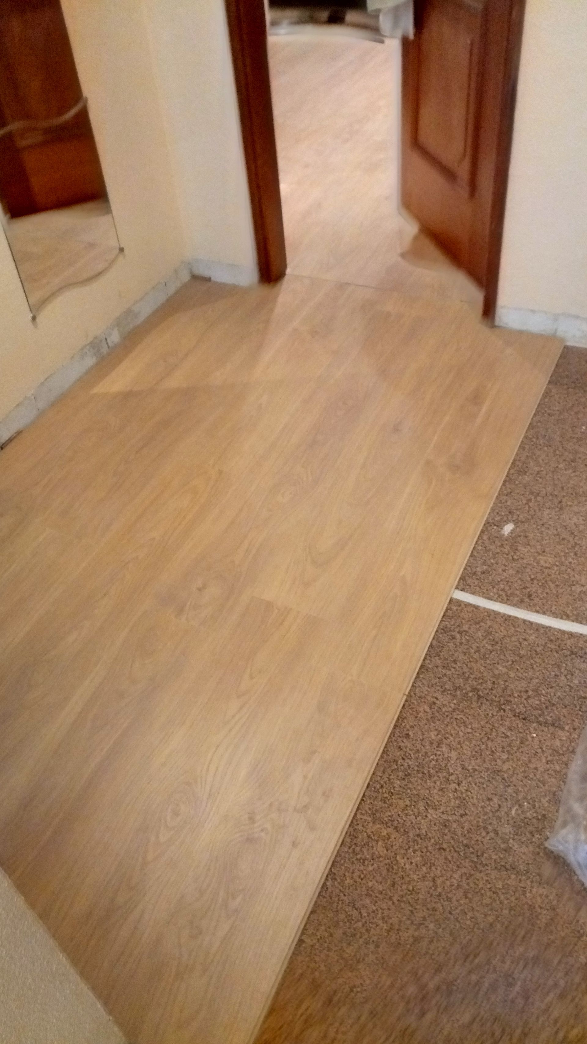 Instalação de piso de madeira clara ao lado do carpete existente na entrada.