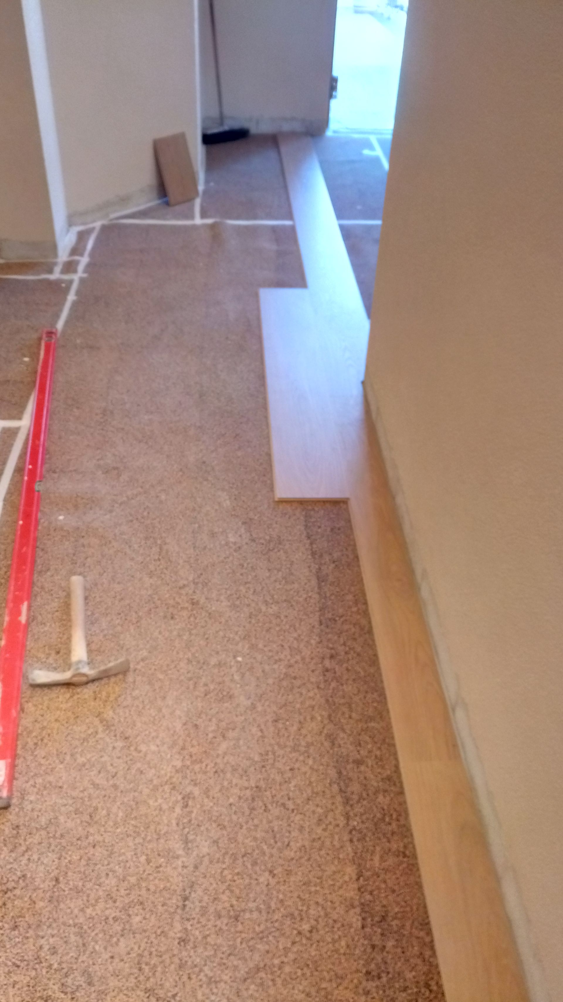 Sala com carpete e piso sendo instalado; um nível e um martelo são visíveis.