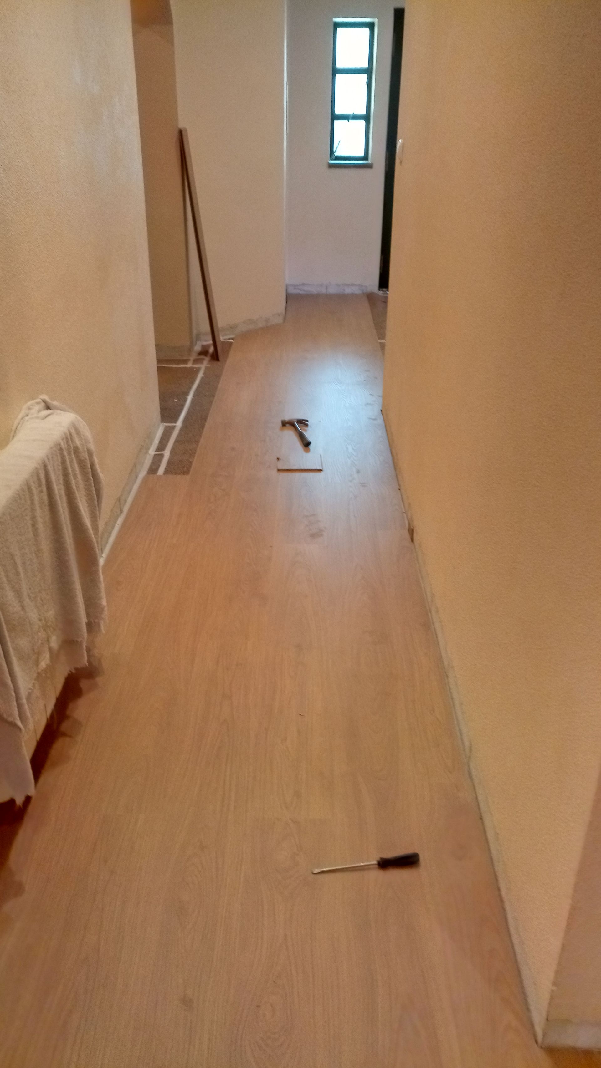 Corredor com piso de madeira em construção, ferramentas no chão. Paredes em bege claro.