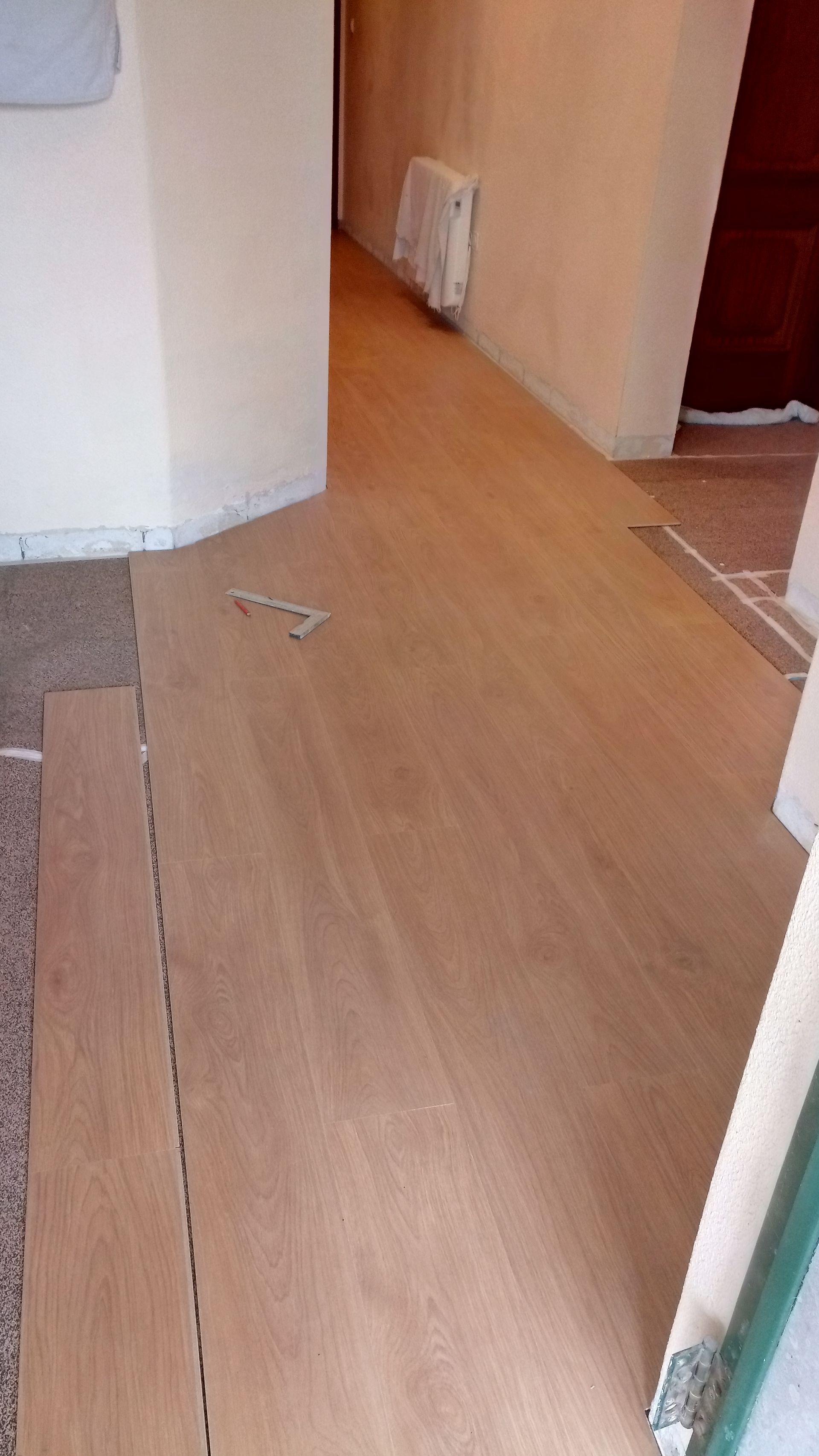 Instalação de piso de madeira em um corredor; paredes bege; porta à direita.