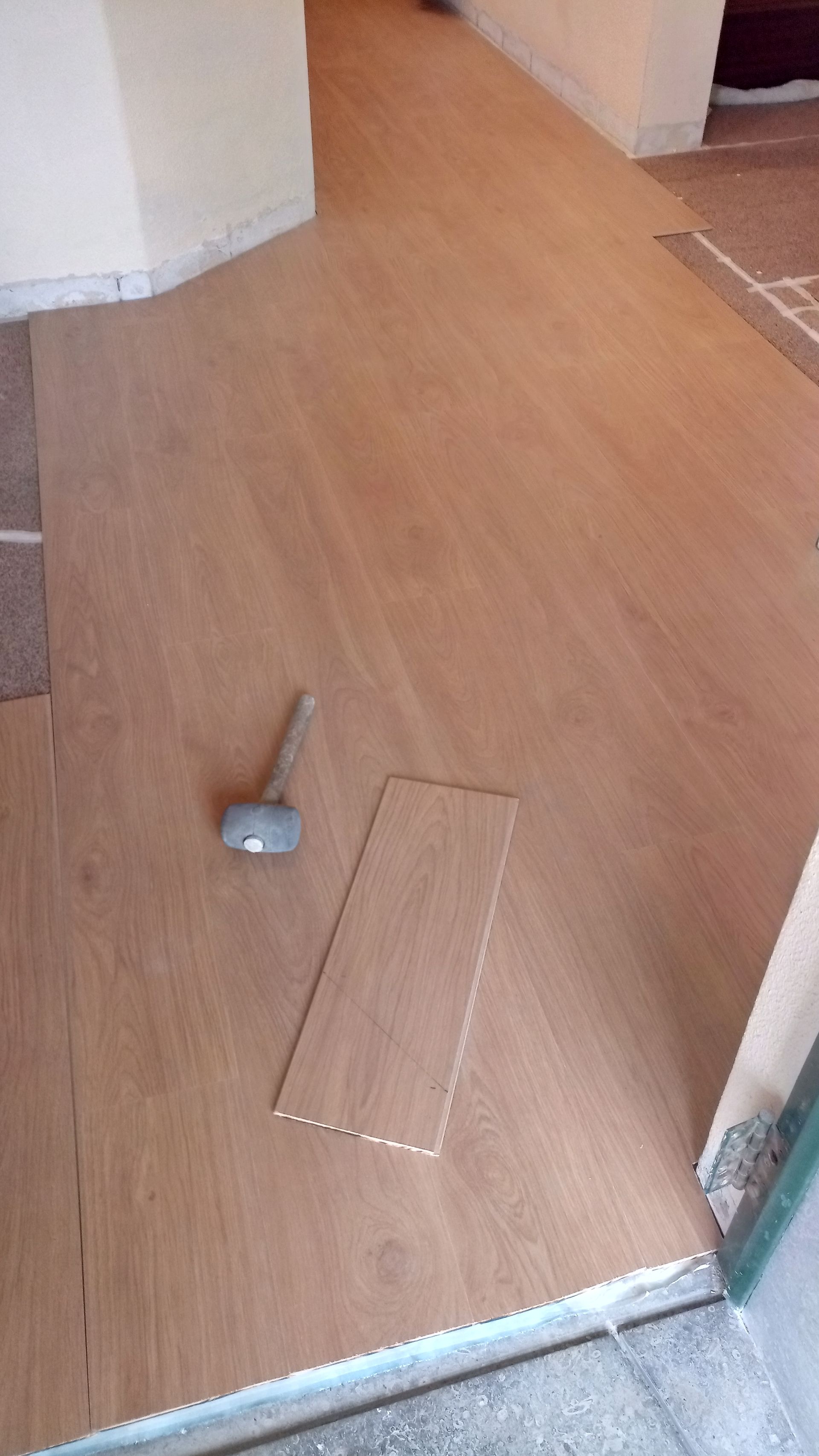 Instalação de piso laminado marrom claro; tábuas marteladas e cortadas por cima.