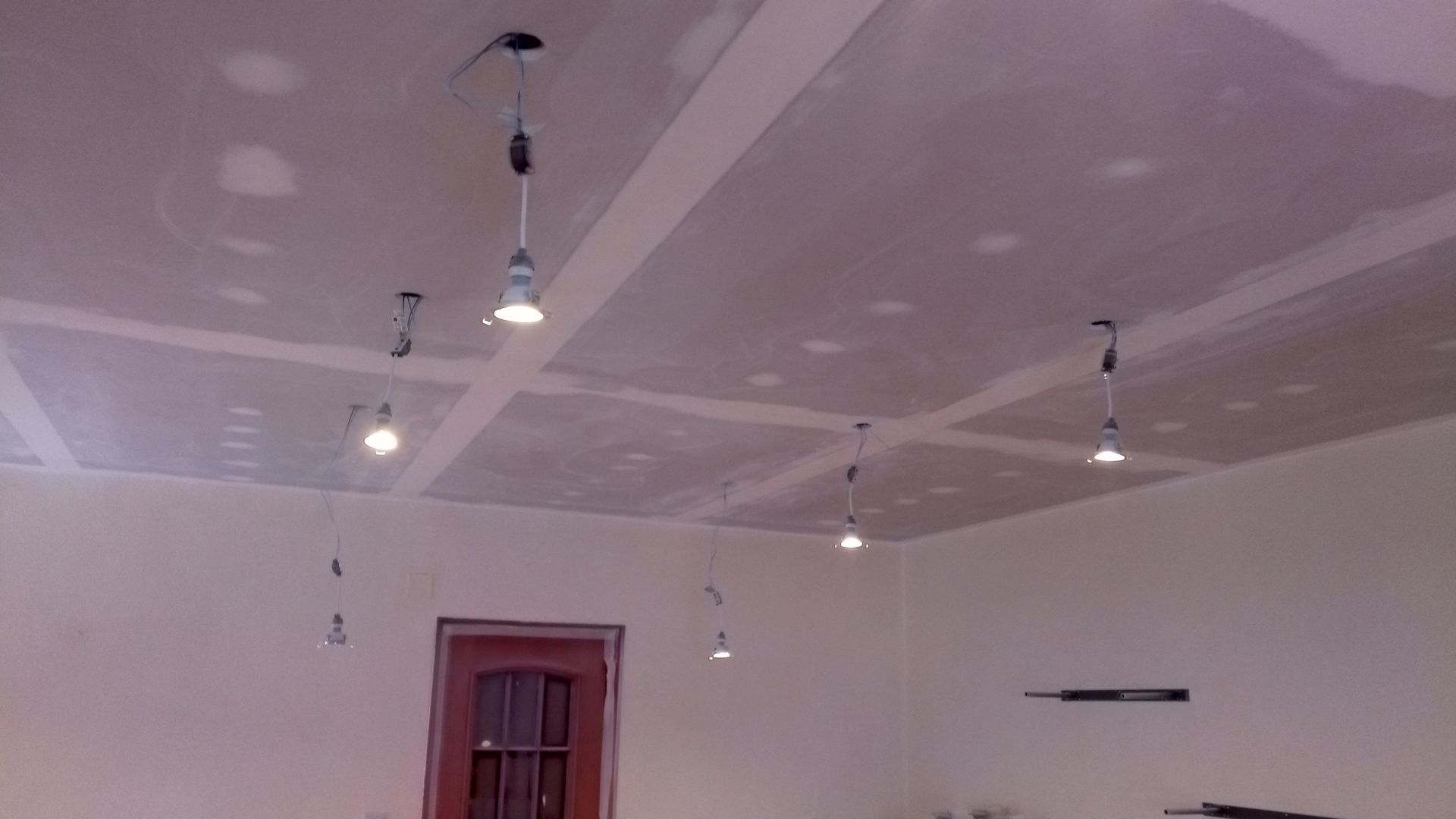 Teto com drywall instalado e luminárias pendentes aparentes. Cômodo em construção.