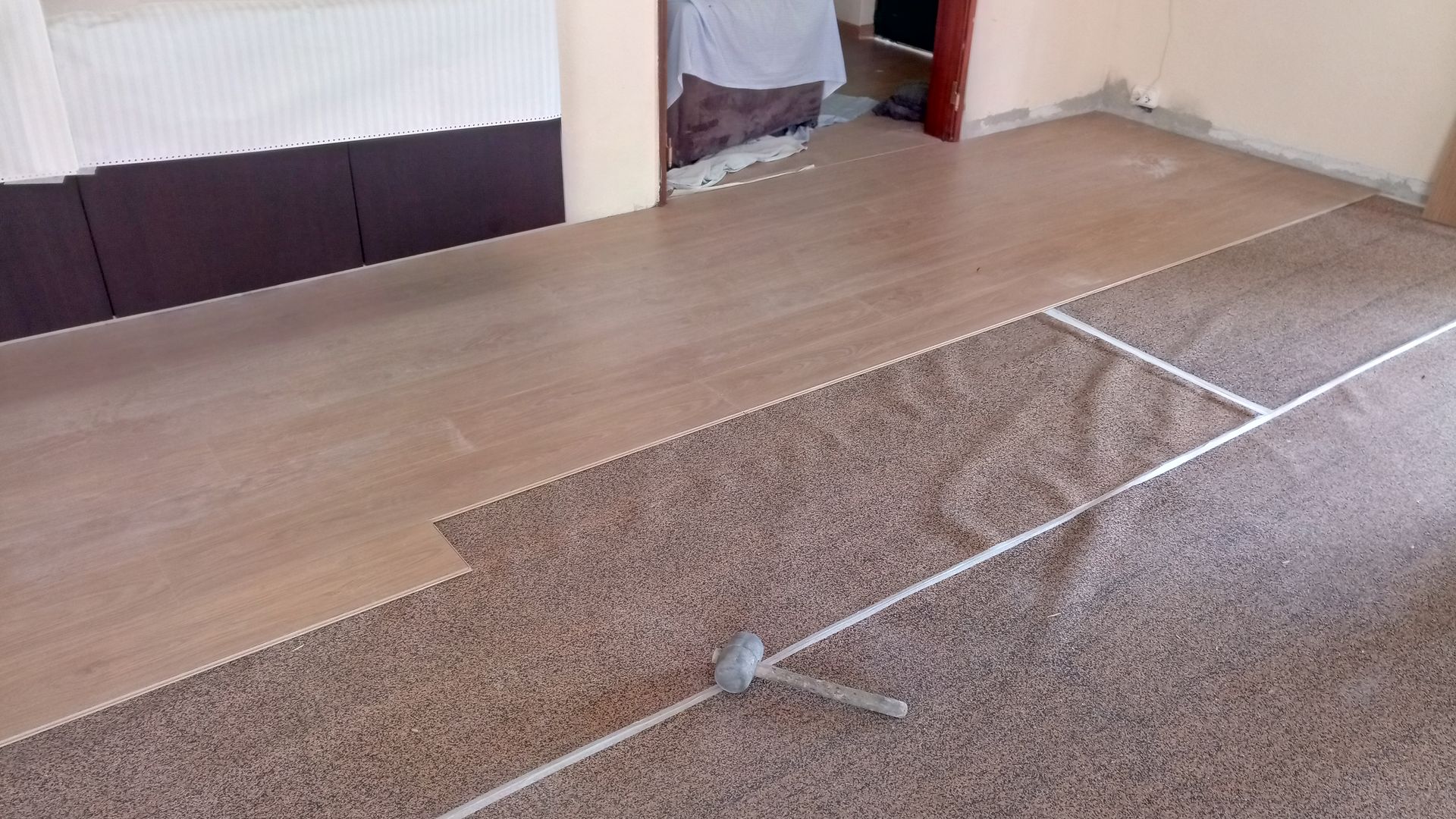 Instalação de piso de madeira sobre carpete, em ambiente interno.