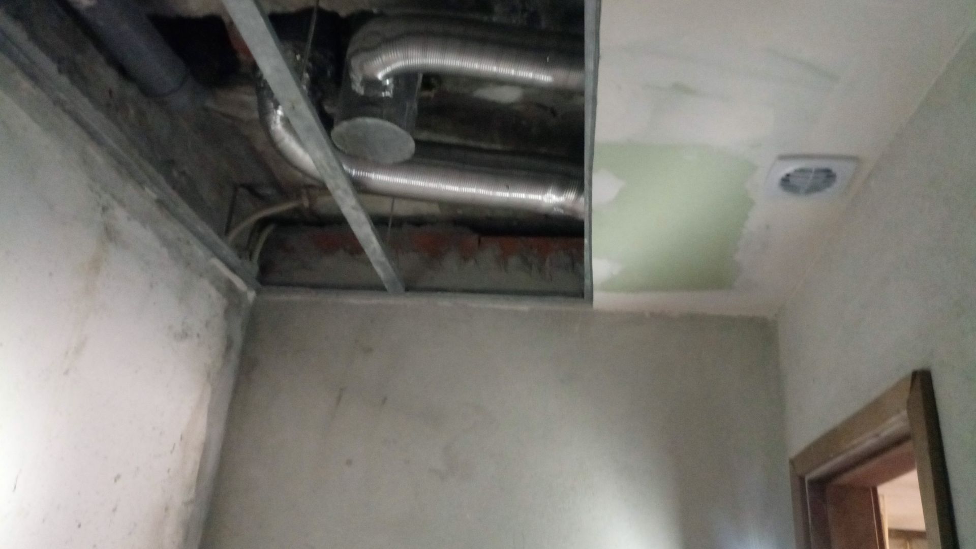 Teto em construção, mostrando a tubulação de ar condicionado, a estrutura metálica e um remendo de drywall parcialmente acabado.