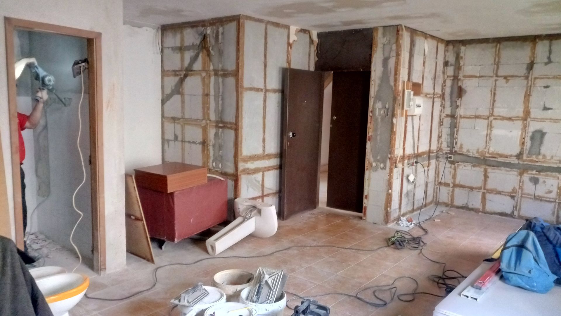 Interior de um cômodo em reforma; paredes expostas, portas abertas, ferramentas e uma pessoa trabalhando.