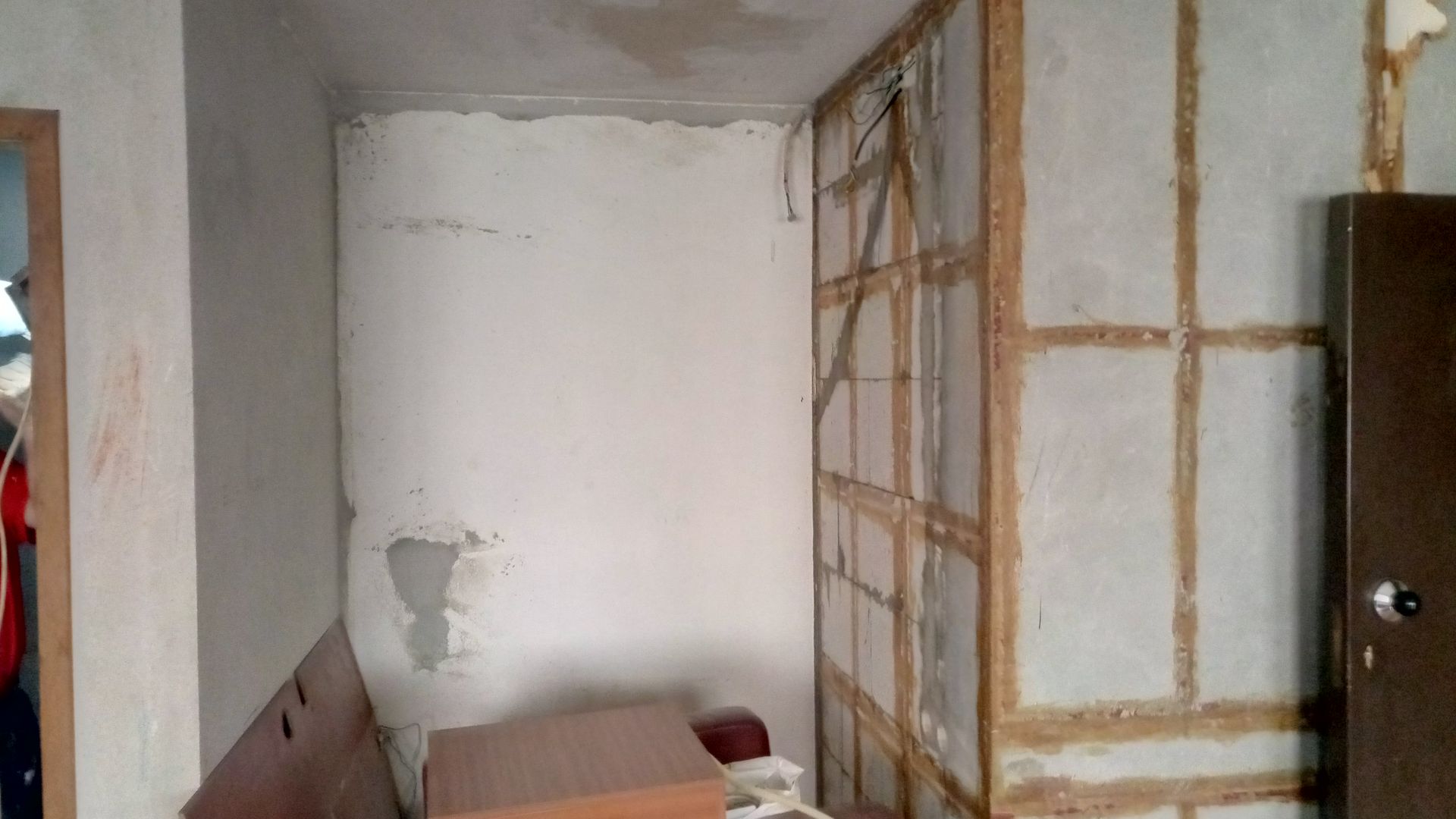 Vista interior de um cômodo em reforma. Paredes danificadas com estrutura de madeira exposta.