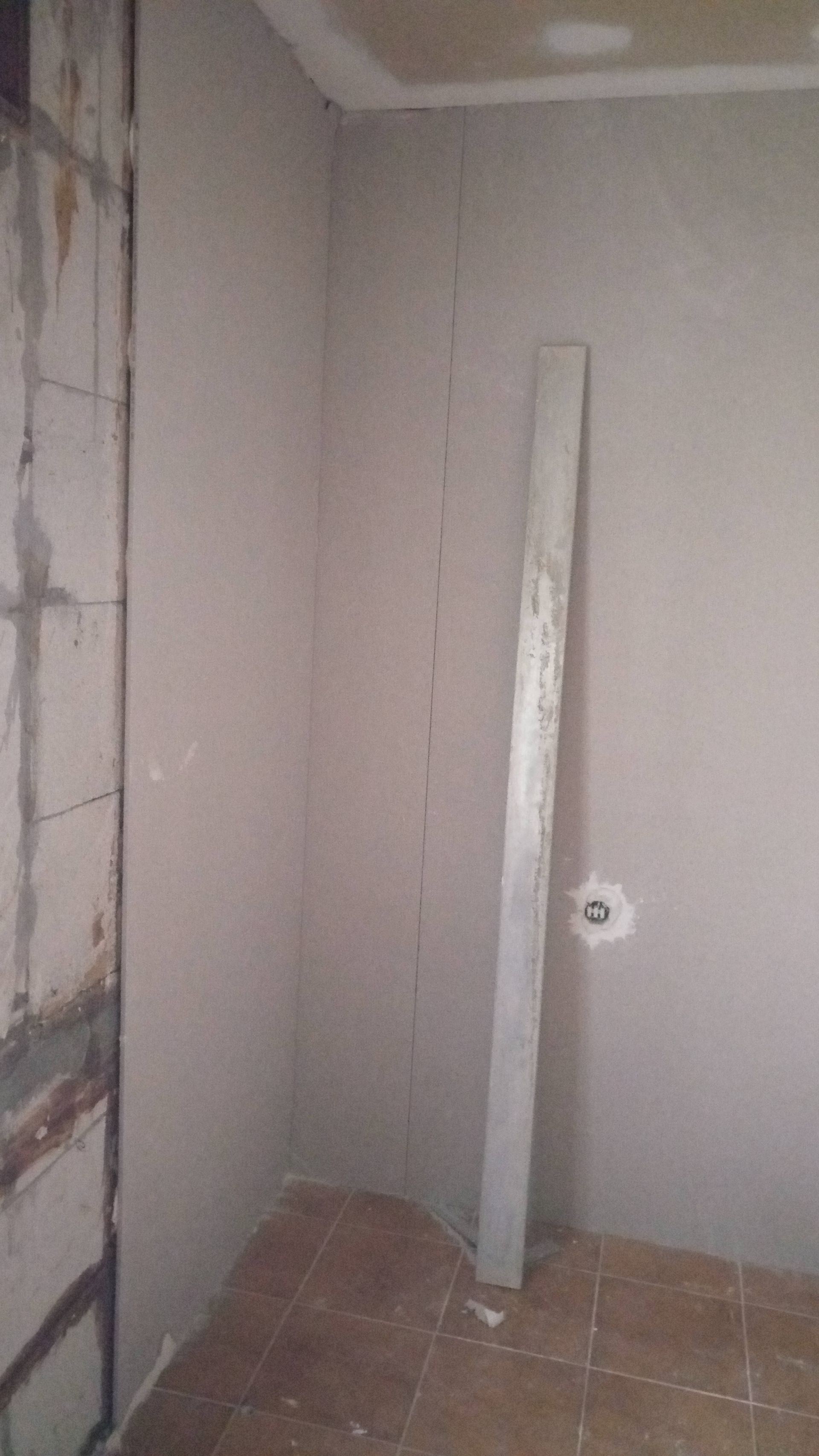 Canto de cômodo interno com paredes inacabadas, um nível encostado na parede e piso de azulejo.