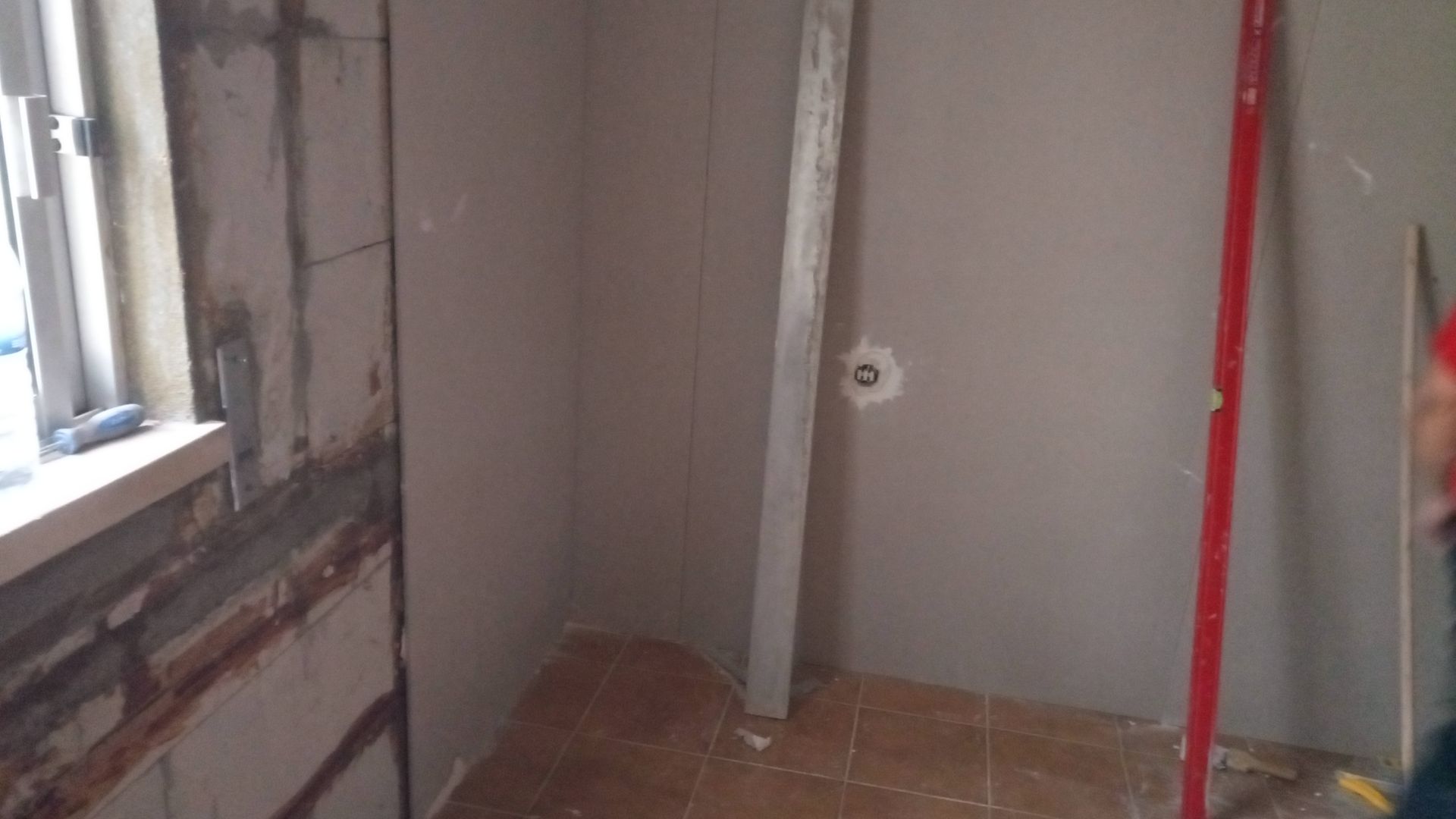 Interior de um canteiro de obras, mostrando paredes inacabadas com drywall e uma instalação hidráulica.
