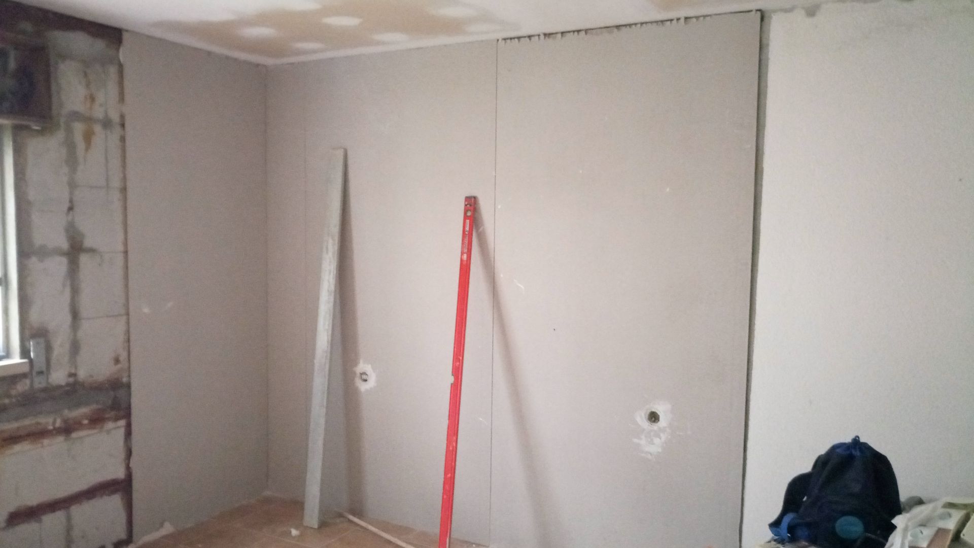 Interior de um cômodo com instalação de drywall em andamento; paredes inacabadas, niveladas e com materiais visíveis.