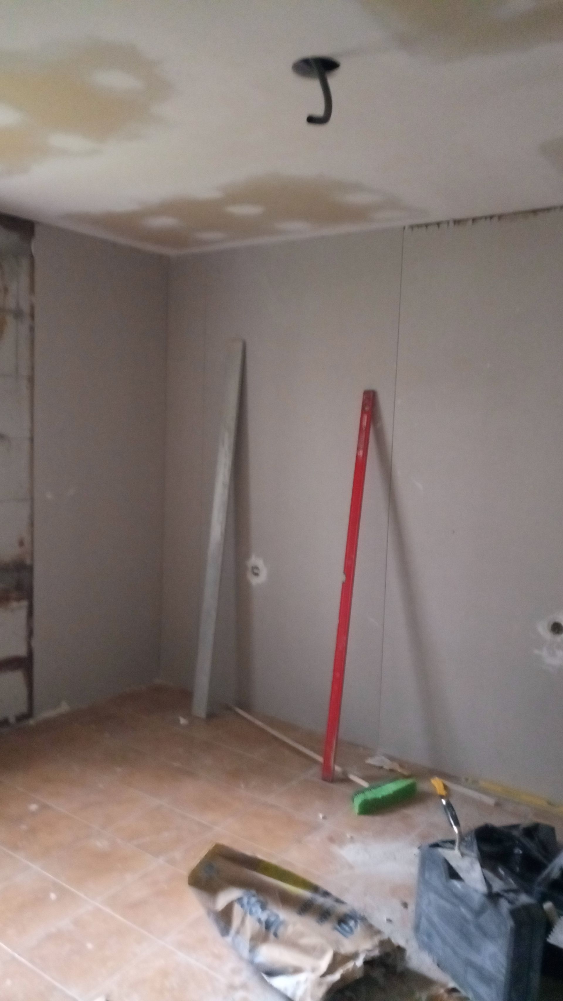 Quarto em reforma com drywall, ferramentas e um gancho no teto.