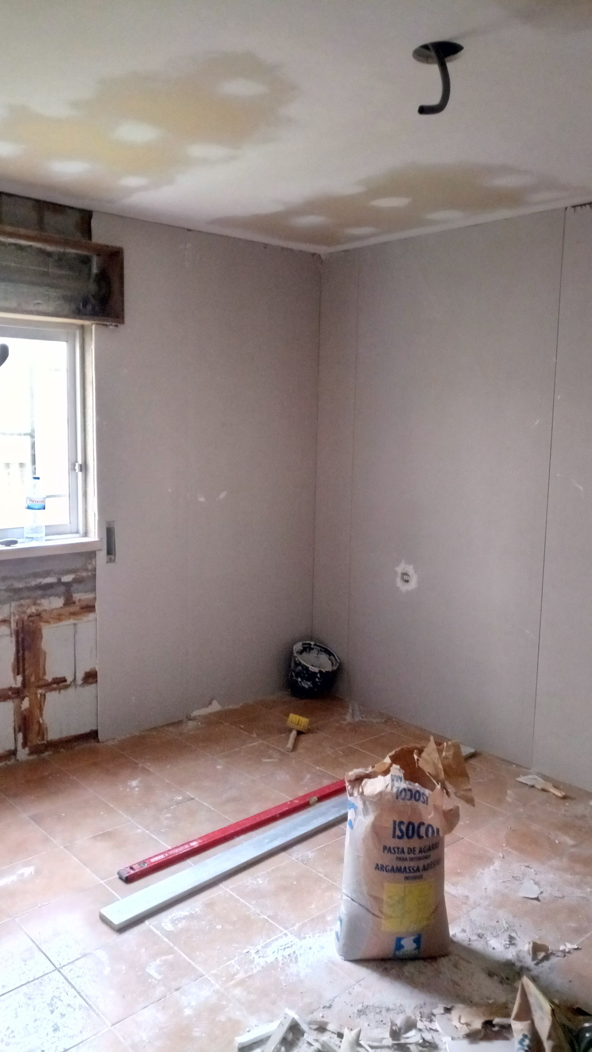 Quarto em reforma com drywall, vigas expostas e materiais de construção à mostra.