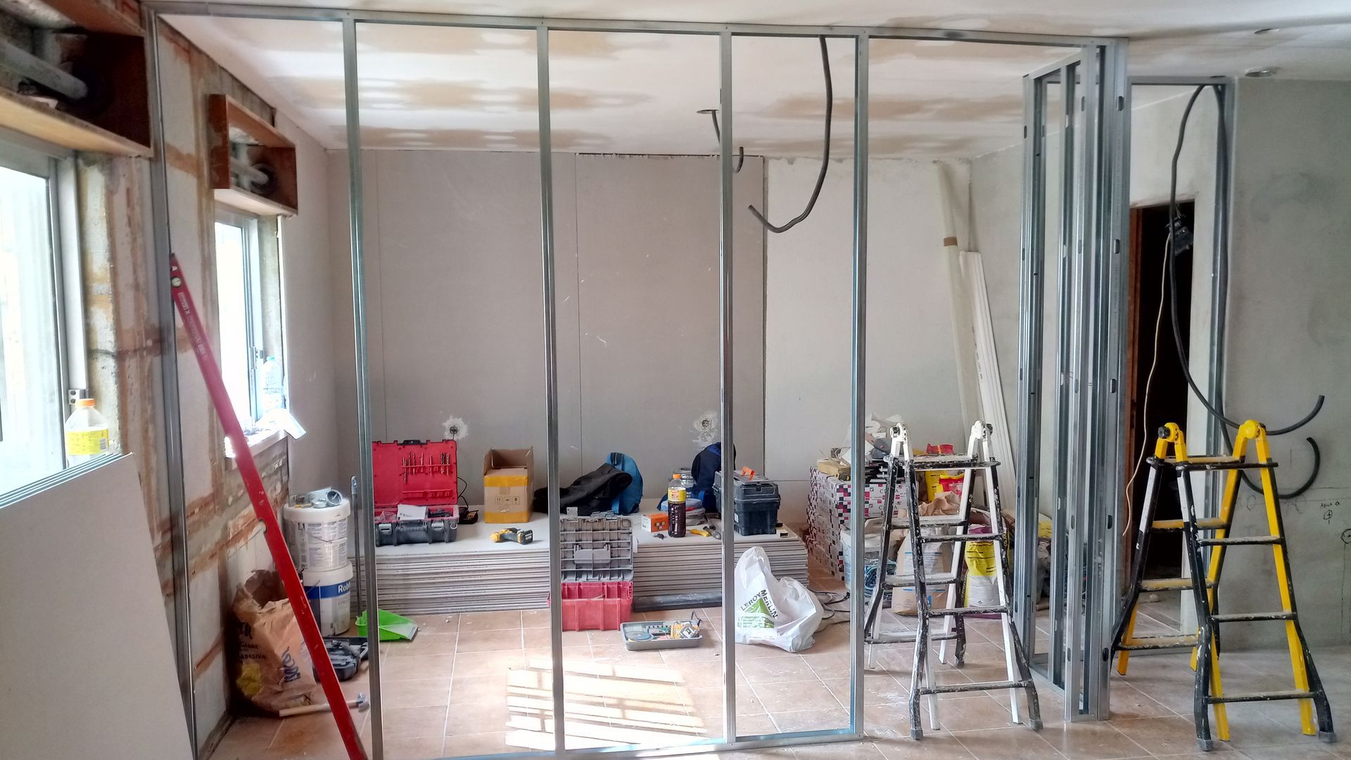 Interior em reforma; estrutura metálica para uma nova parede; ferramentas e materiais espalhados pelo chão.