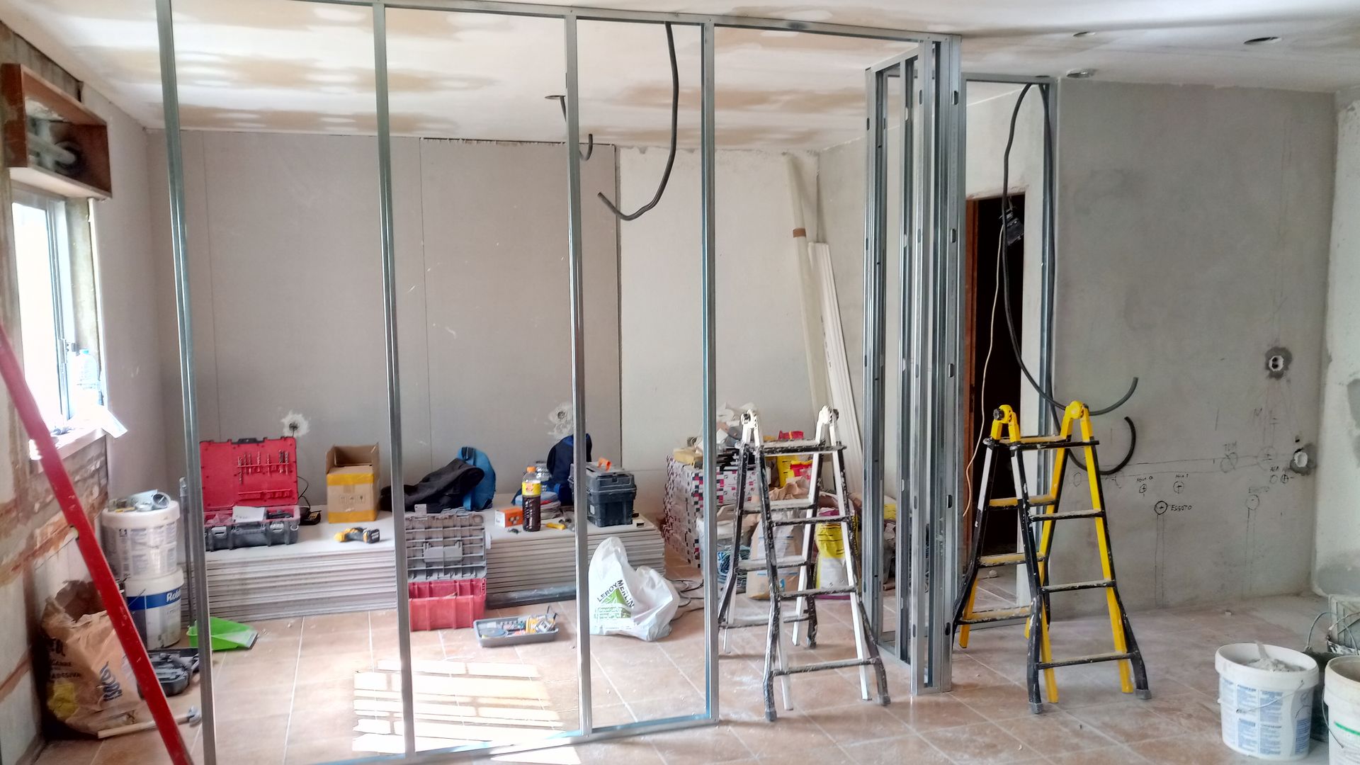 Cena interna de uma obra com estrutura de metal, ferramentas e escadas visíveis.