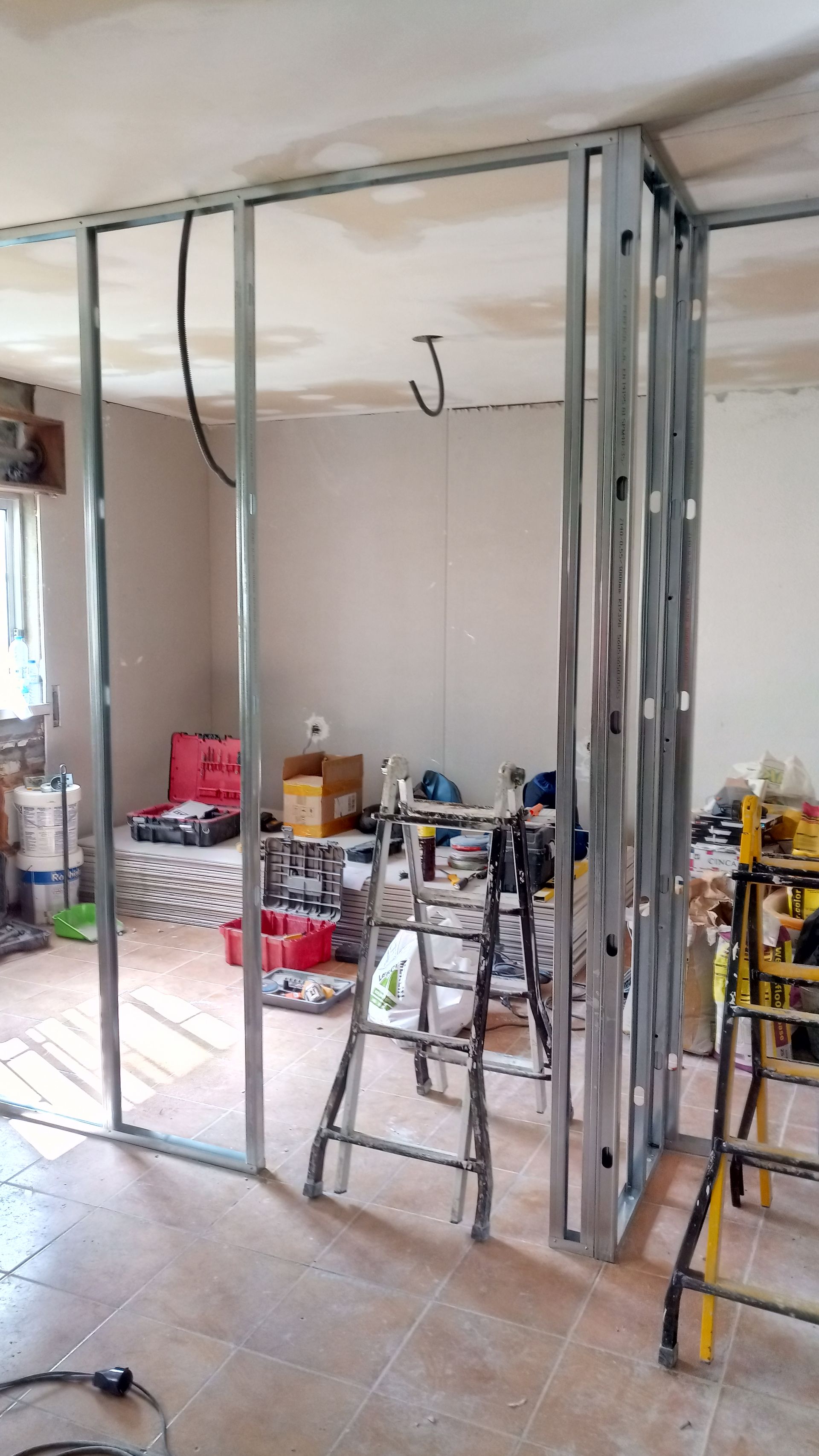 Estrutura metálica de uma parede interna recém-construída em um cômodo. Ferramentas e materiais de construção espalhados ao redor.