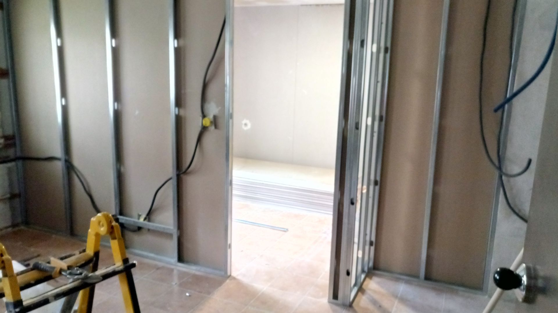 Quarto interno em construção, com estrutura metálica e drywall parcialmente instalado. Fiação elétrica visível.