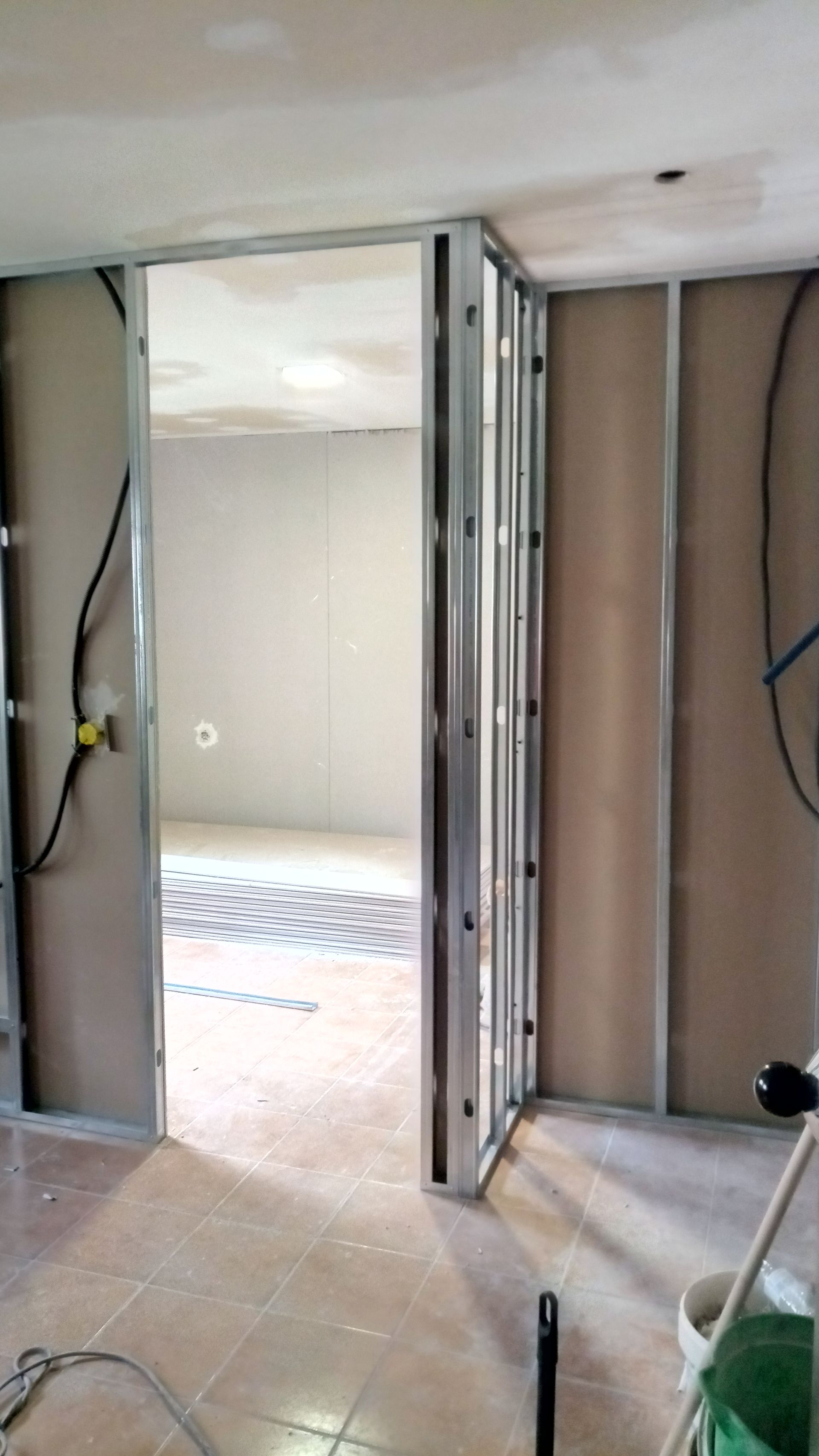 Estrutura metálica delimitando uma porta em construção. Paredes com drywall instalado, fiação elétrica visível.