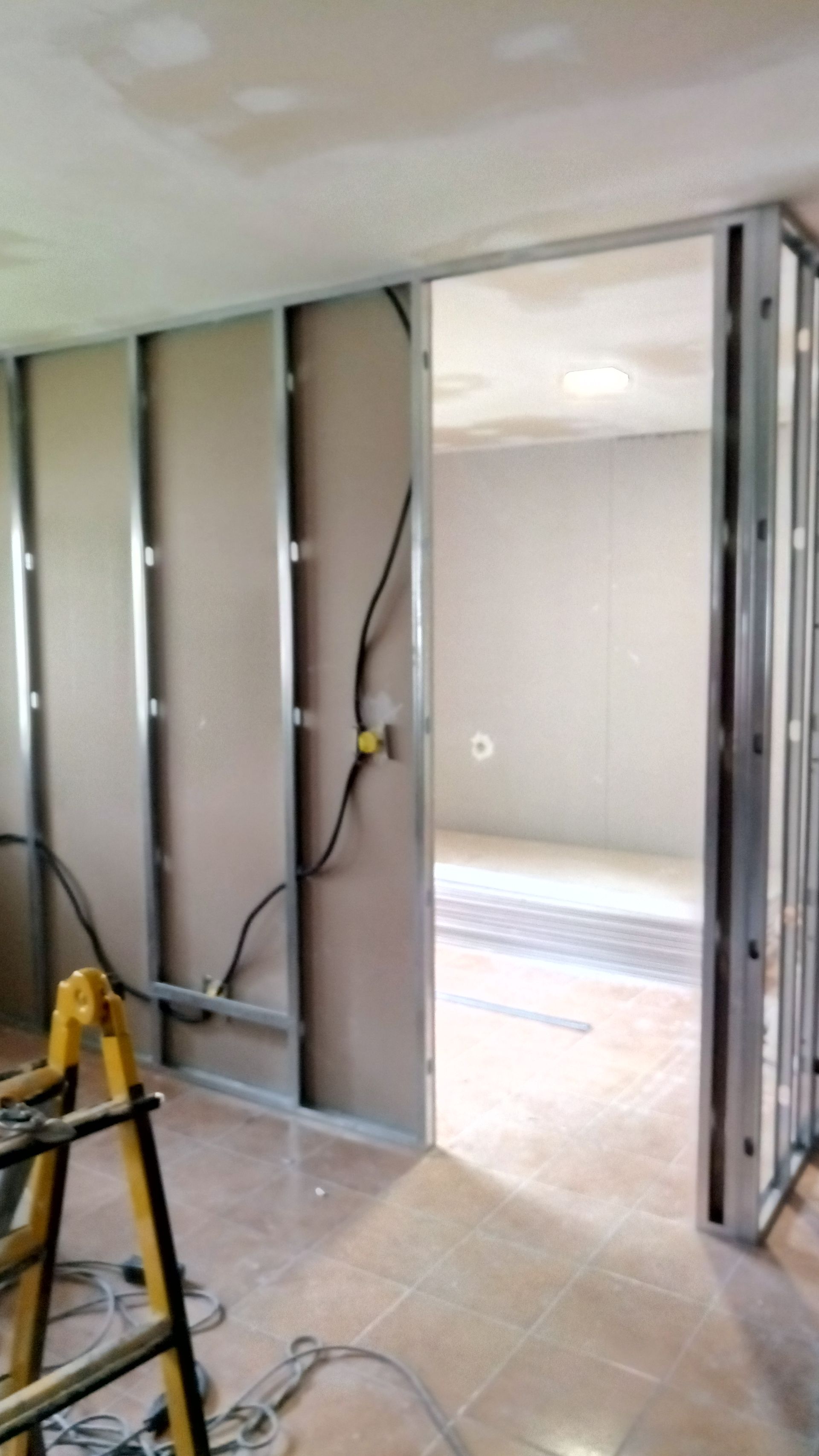 Construção interna: Estrutura metálica com drywall parcialmente instalado, porta de acesso a outro cômodo.