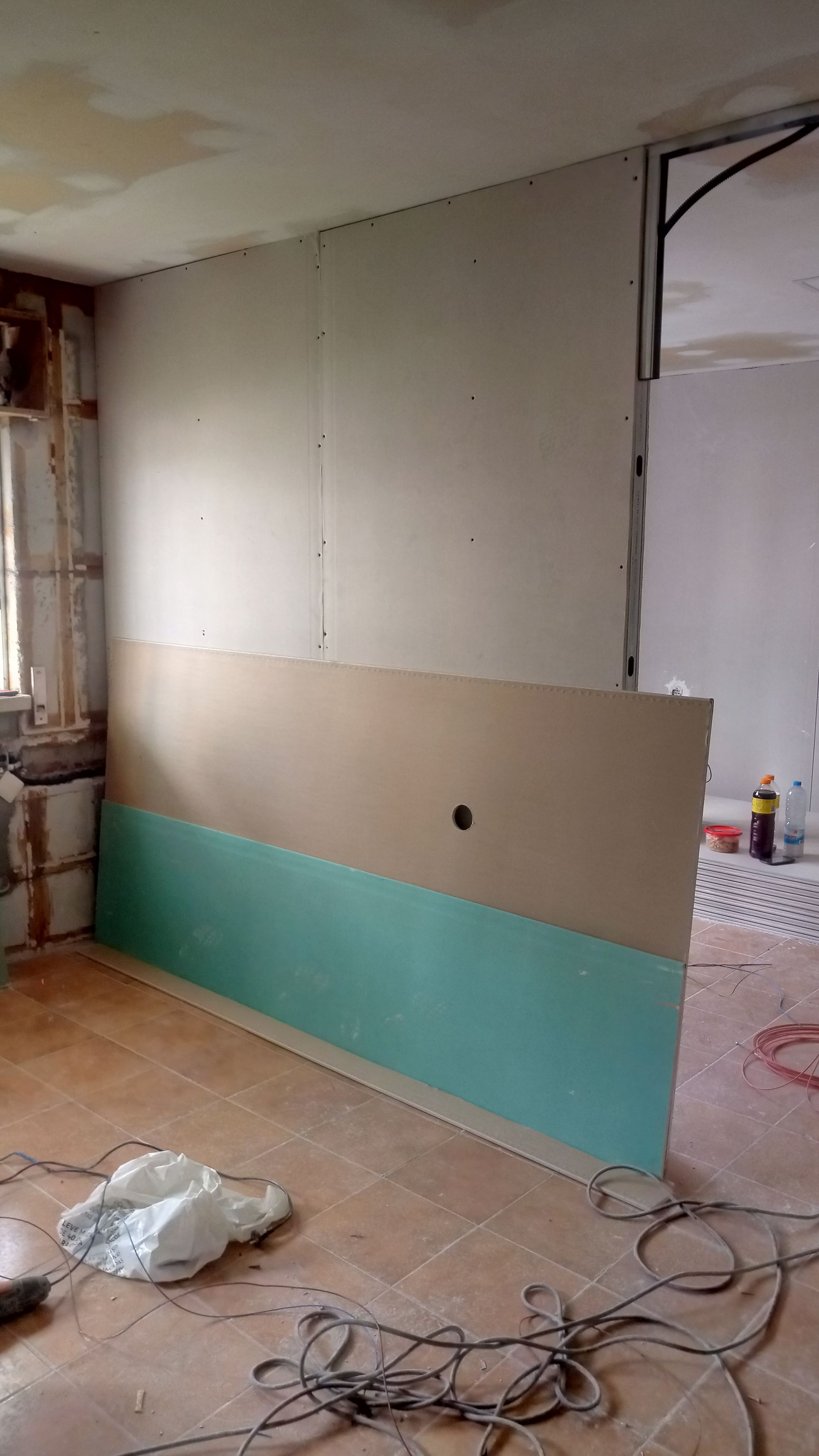 Instalação de drywall em um cômodo, com painéis azuis, bege e brancos. Entulho de construção no chão.