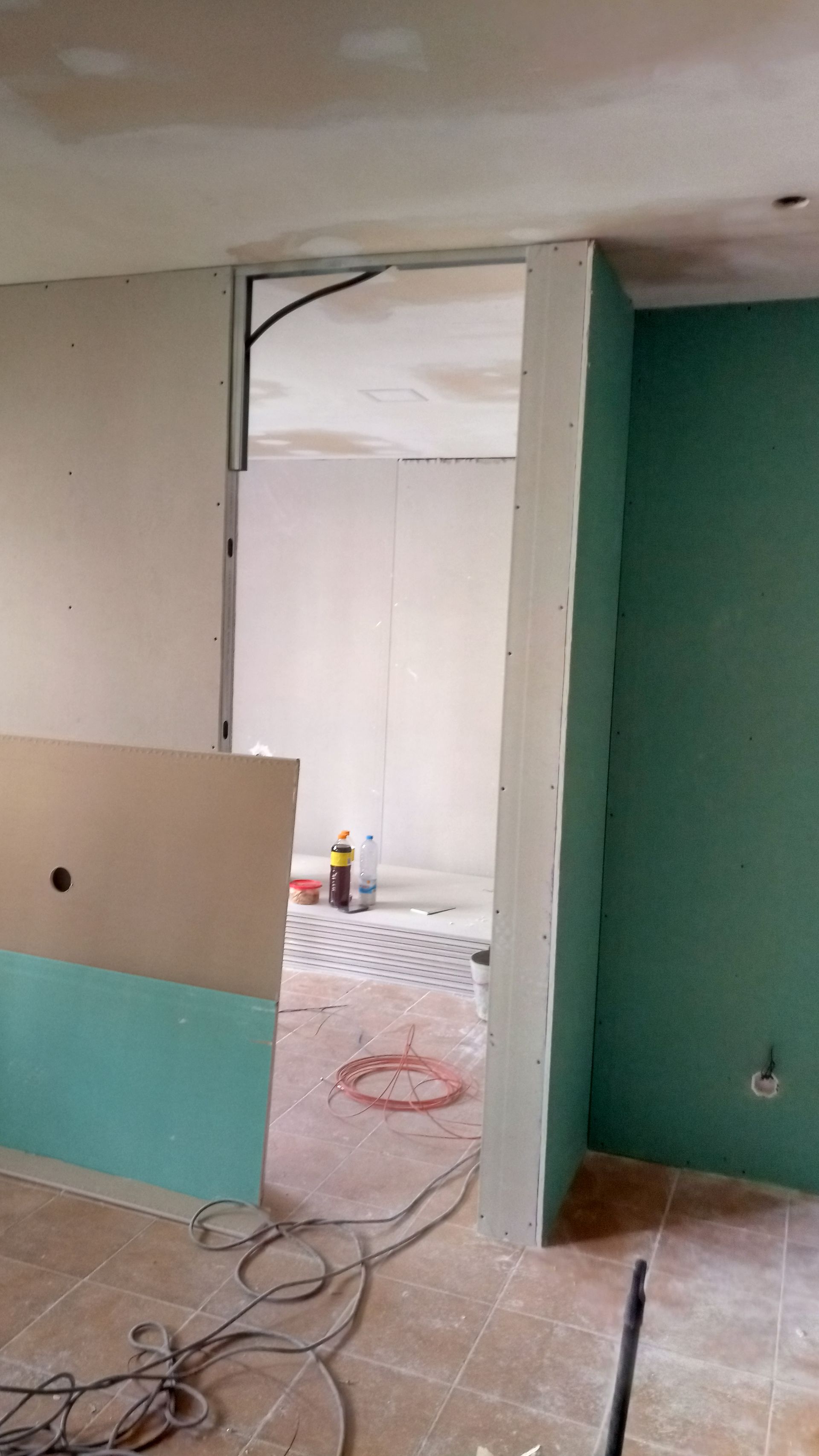 Interior em construção: porta de entrada com estrutura metálica, drywall instalado, paredes verdes, piso sem acabamento.