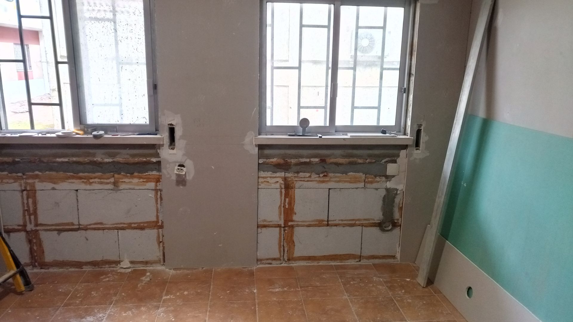 Quarto em reforma, duas janelas. Paredes remendadas, blocos expostos abaixo das janelas, moldura encostada na parede.