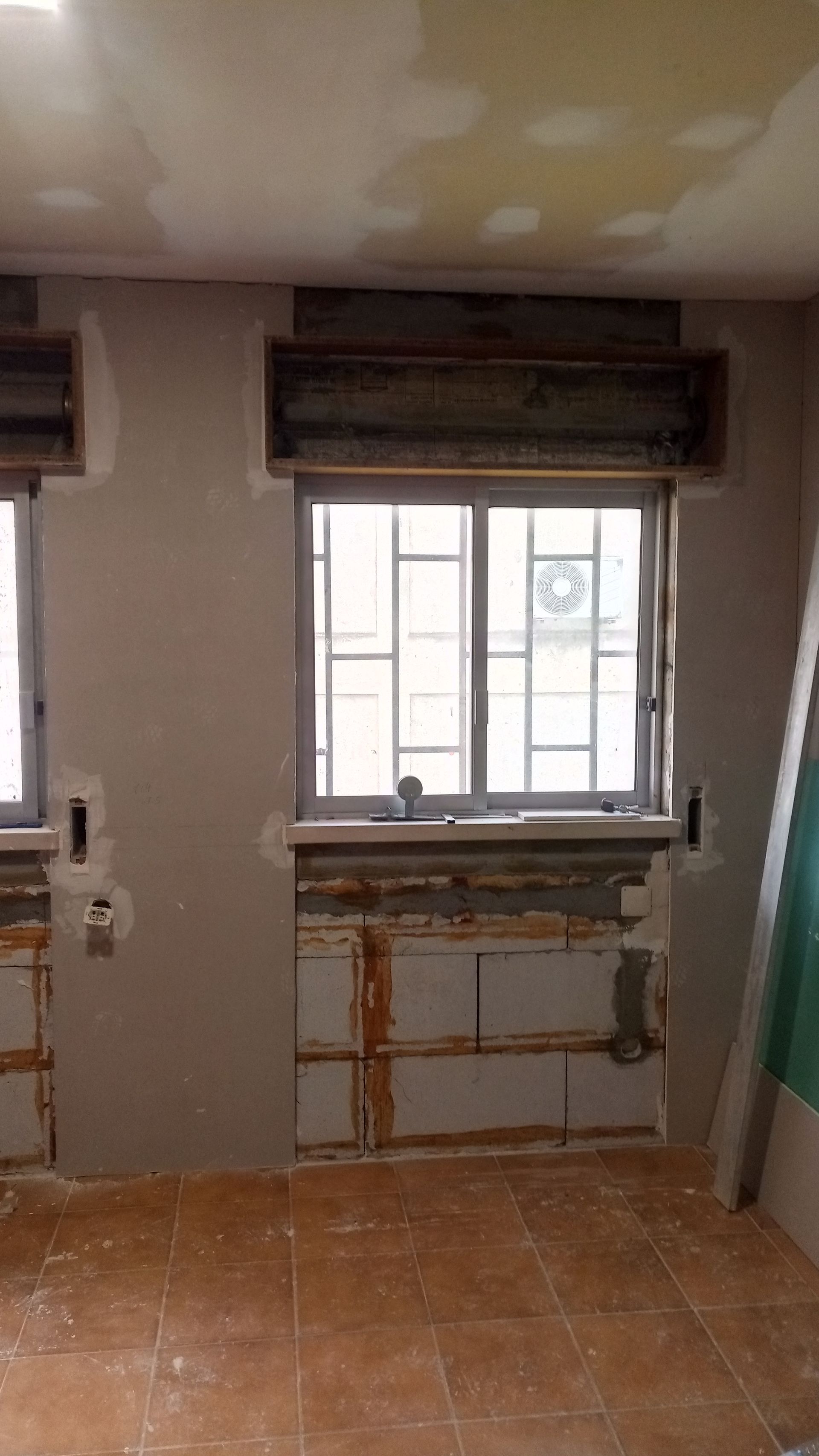 Quarto em reforma com janelas, tijolos aparentes e paredes inacabadas.