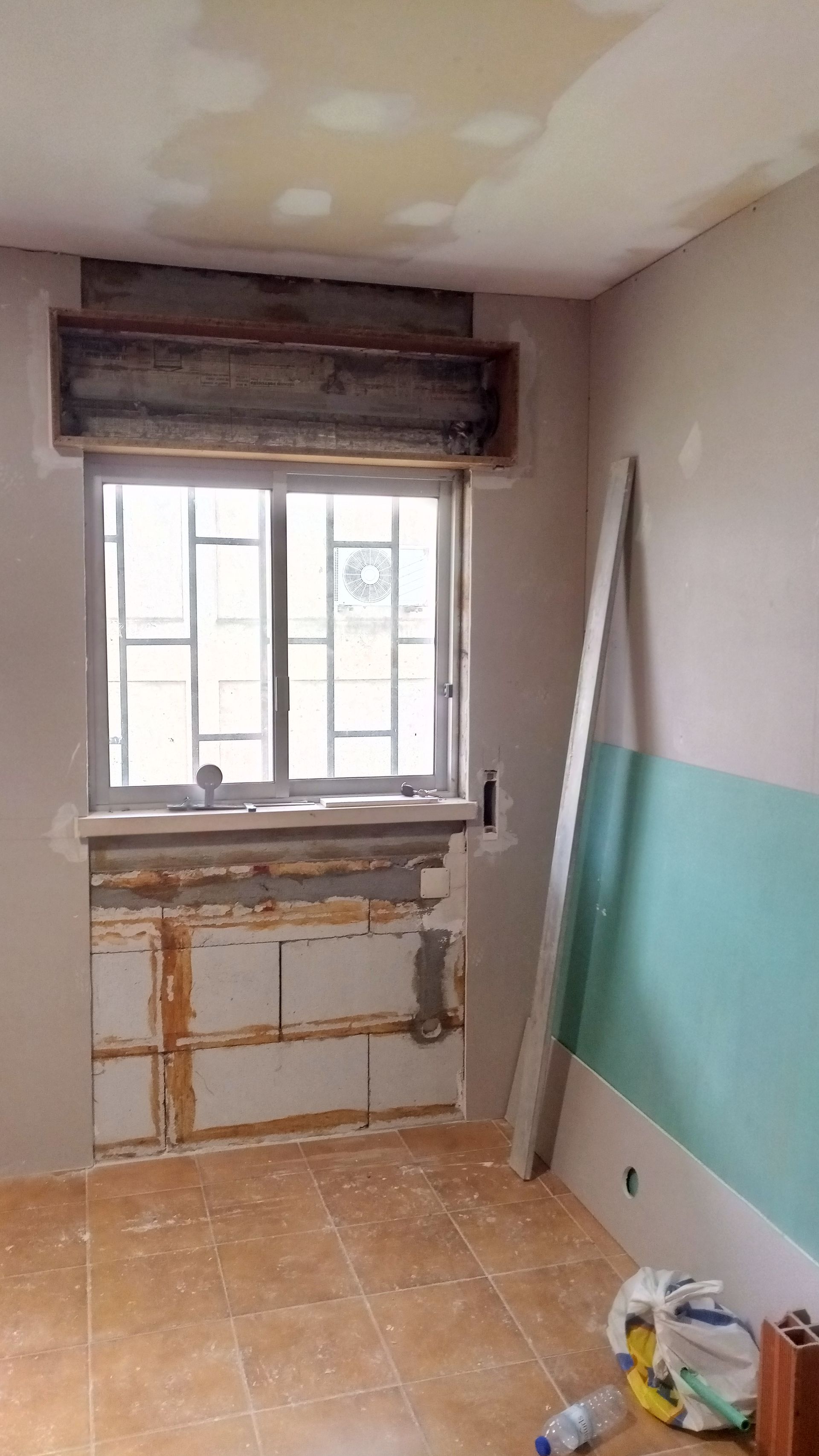 Quarto com interior em reforma, apresentando janela, estrutura aparente e paredes parcialmente pintadas.