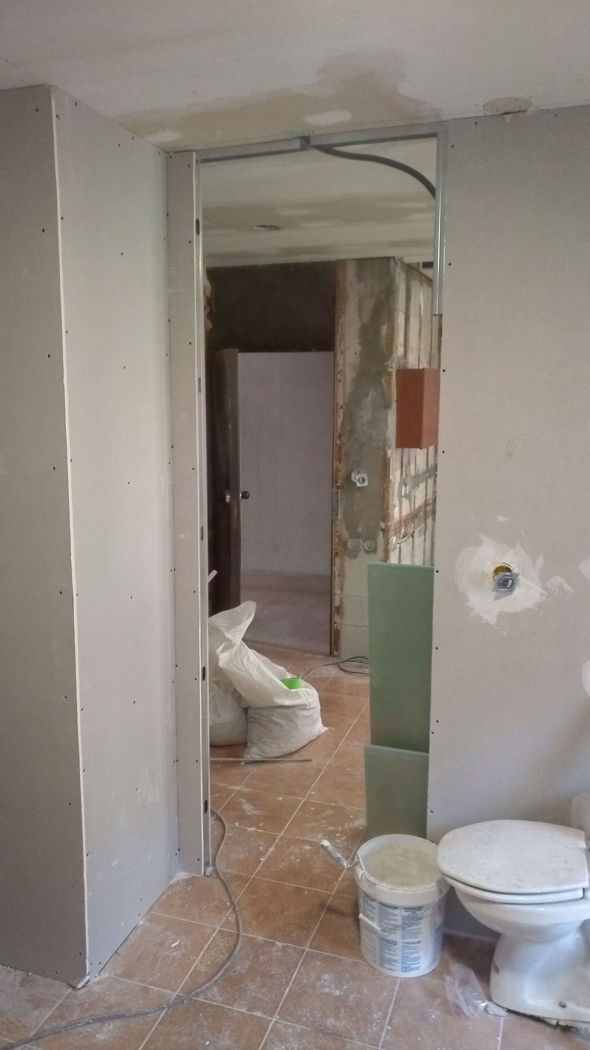 Interior de um cômodo em construção, com estrutura aparente, drywall e um vaso sanitário.