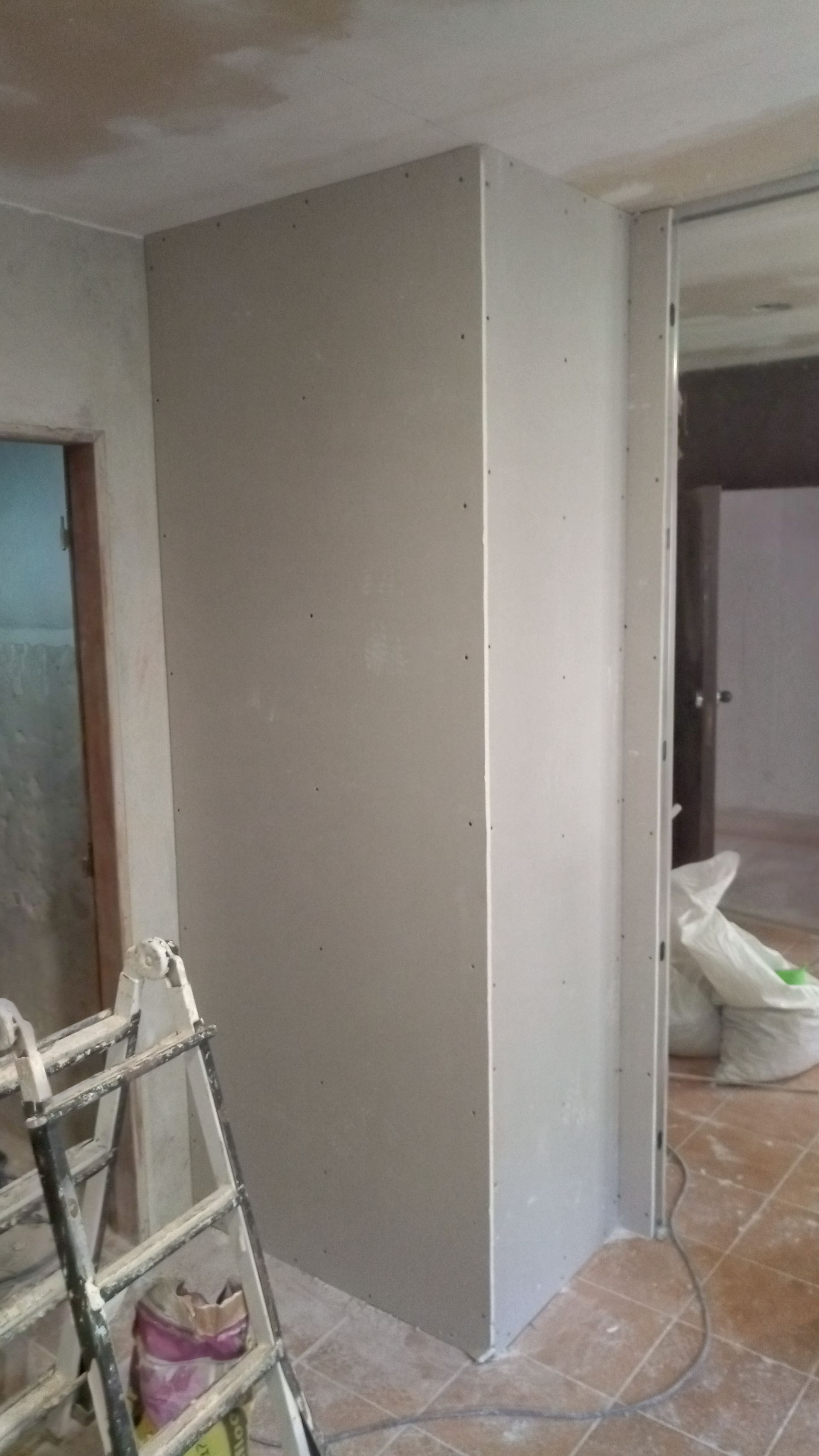 Placa de gesso acartonado instalada em uma parede de canto durante a construção, com escada e porta visíveis.