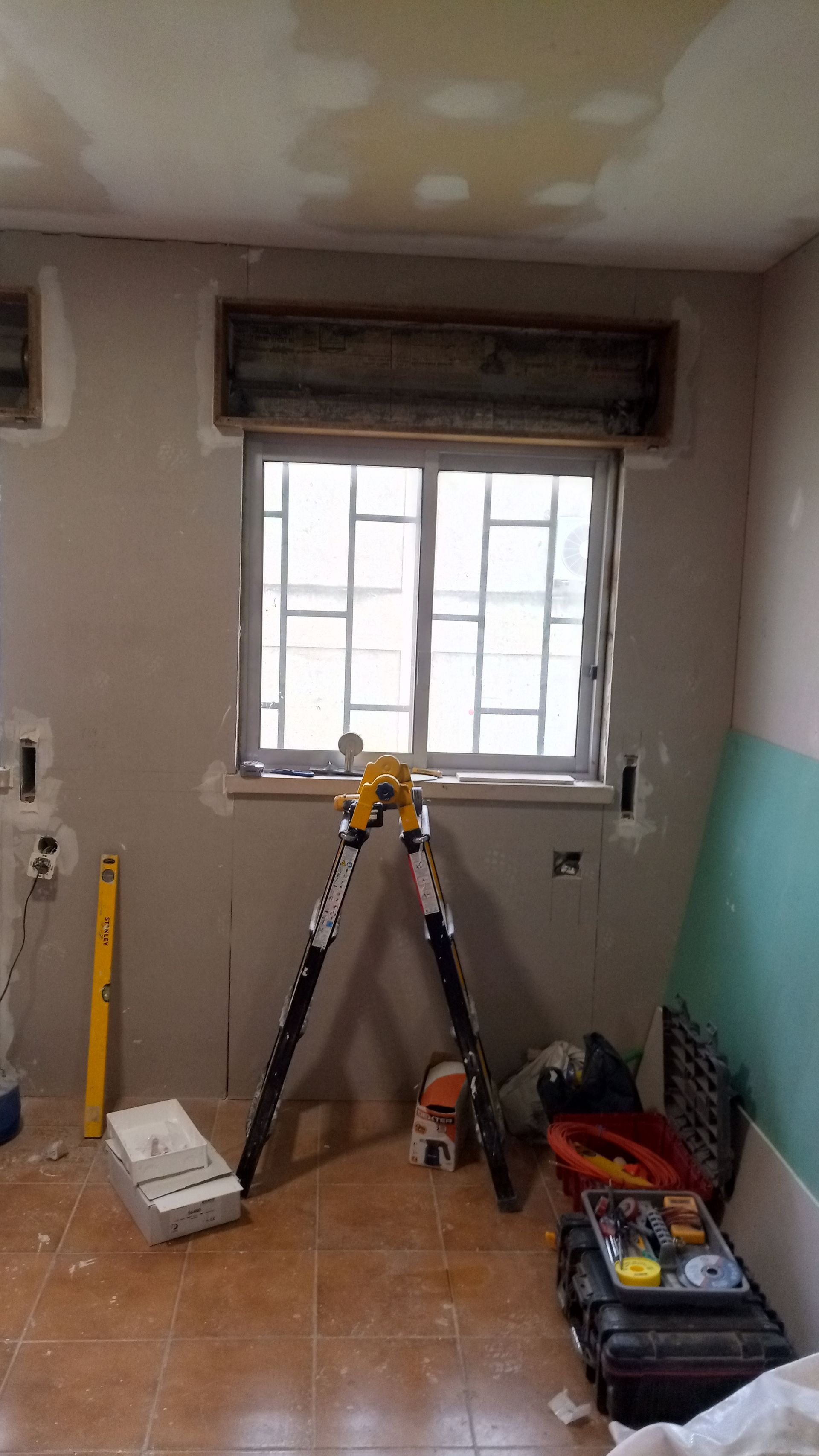 Quarto interior em reforma, janela com grades de segurança, equipamentos de construção na frente.