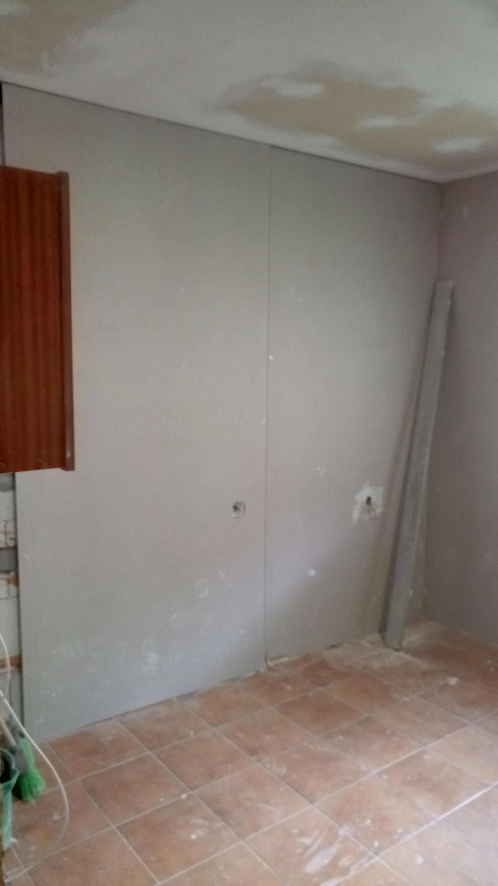 Parede interna com drywall cinza claro; armário marrom, piso de cerâmica marrom e rodapé.
