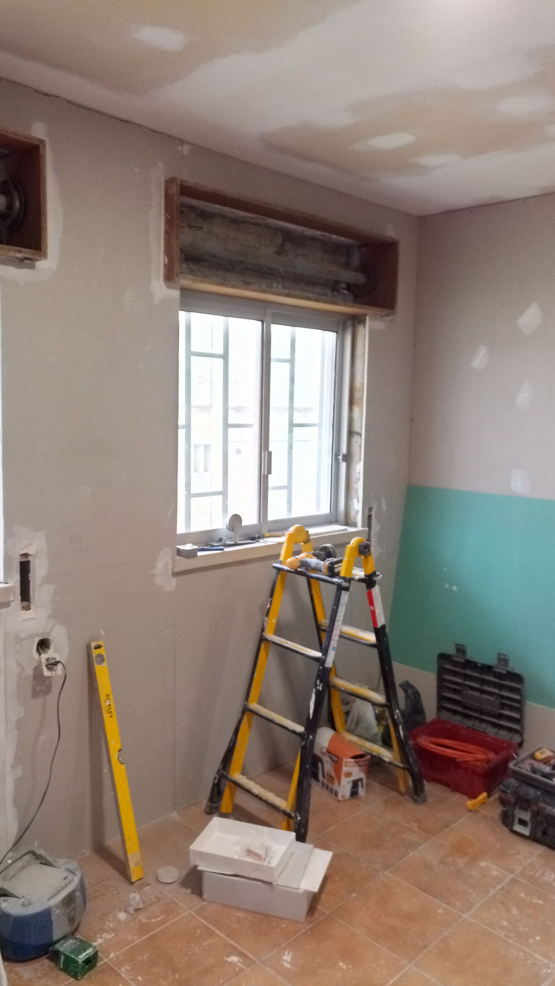 Quarto em reforma com janela, escada, ferramentas e parede exposta.