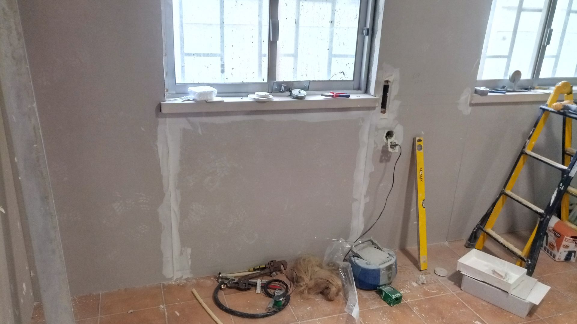 Quarto em construção com janelas, ferramentas e uma escada.