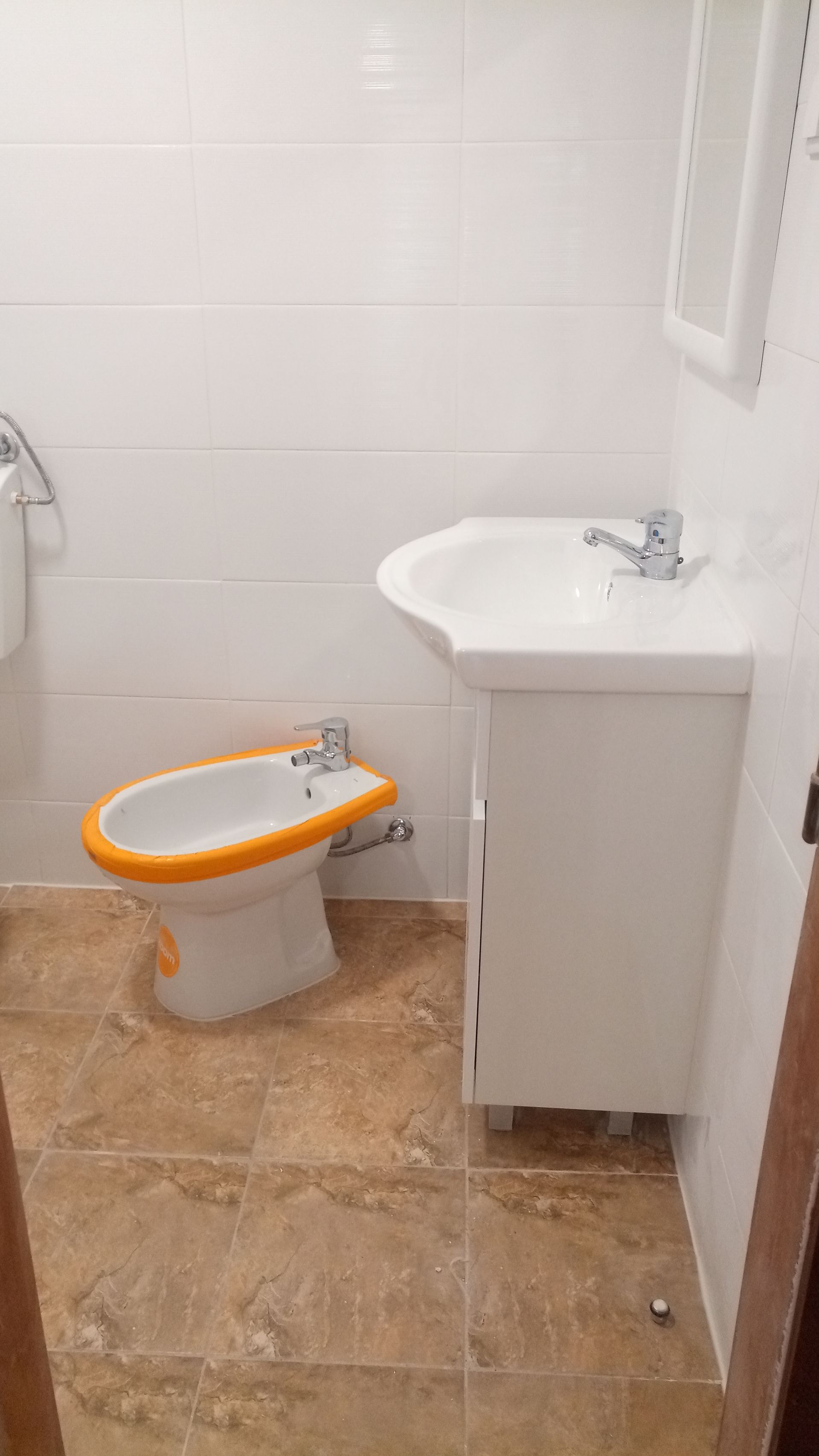 Banheiro com bidê, pia e paredes revestidas com azulejos brancos. Piso bege.