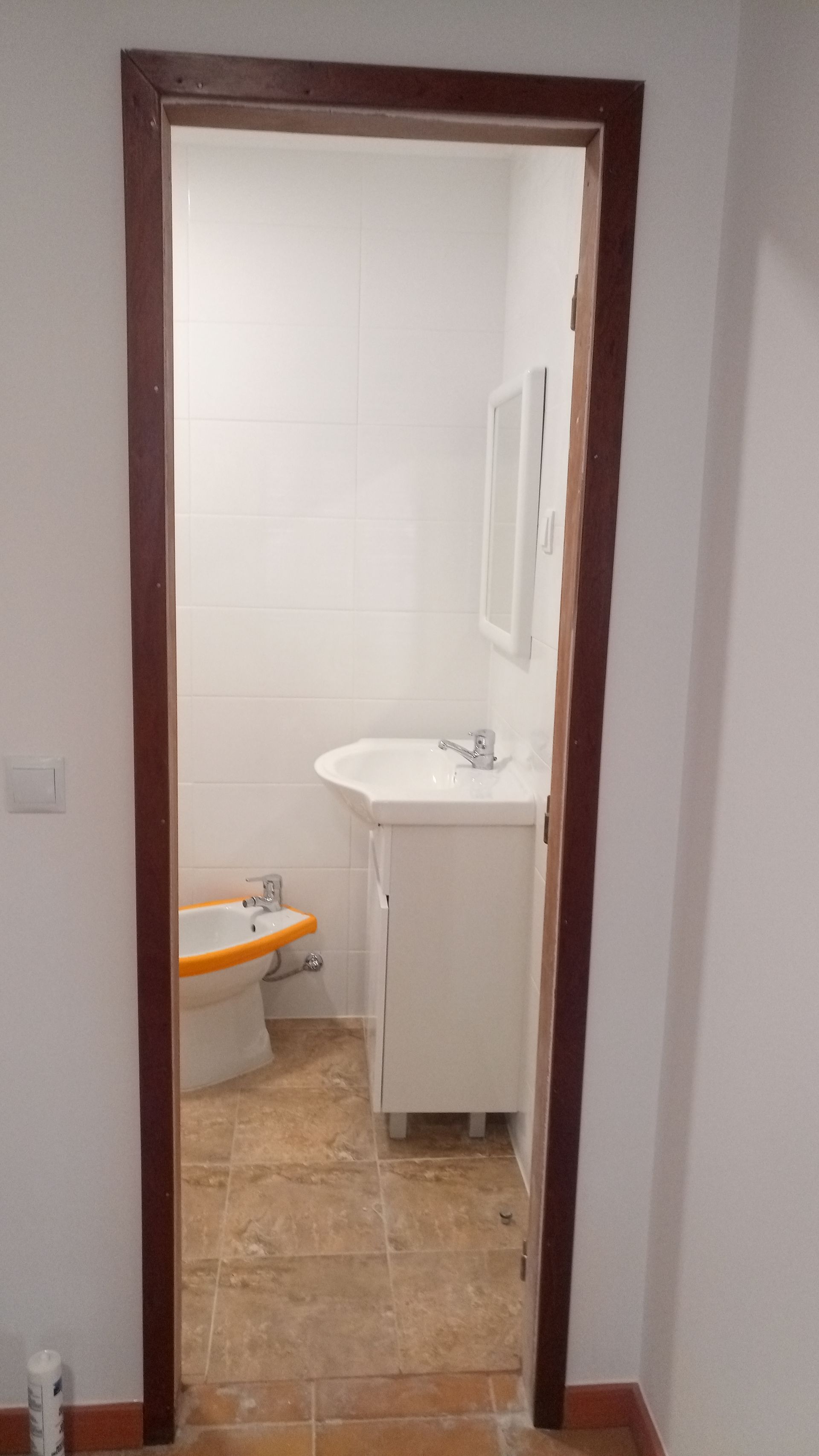 Porta de entrada para um banheiro pequeno com pia, vaso sanitário e espelho. Esquema de cores em branco e marrom.