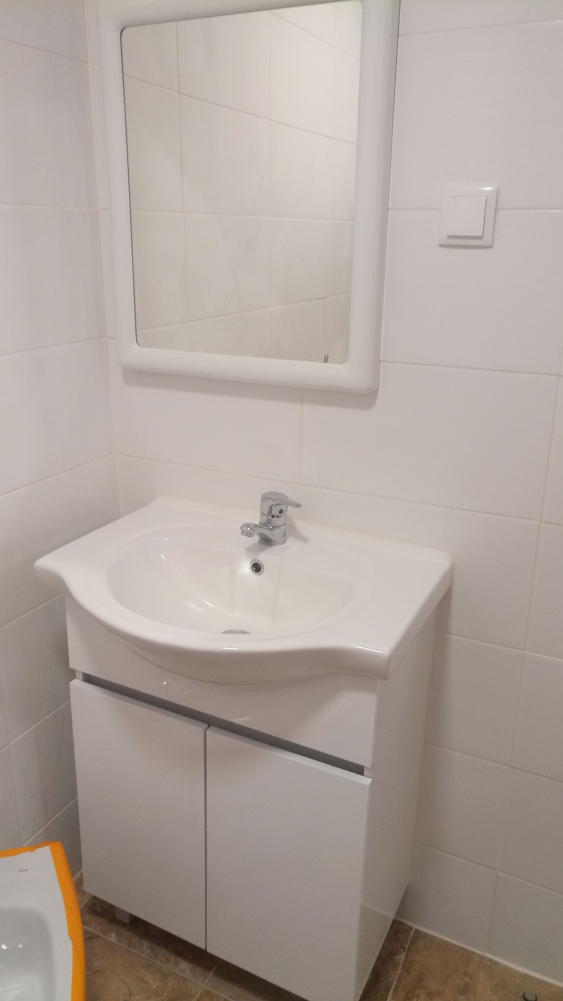 Pia de banheiro branca com armário, espelho e paredes revestidas com azulejos brancos.