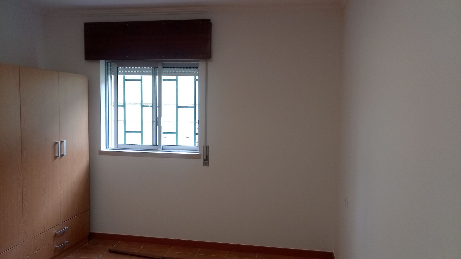 Quarto vazio com janela e armário marrom.