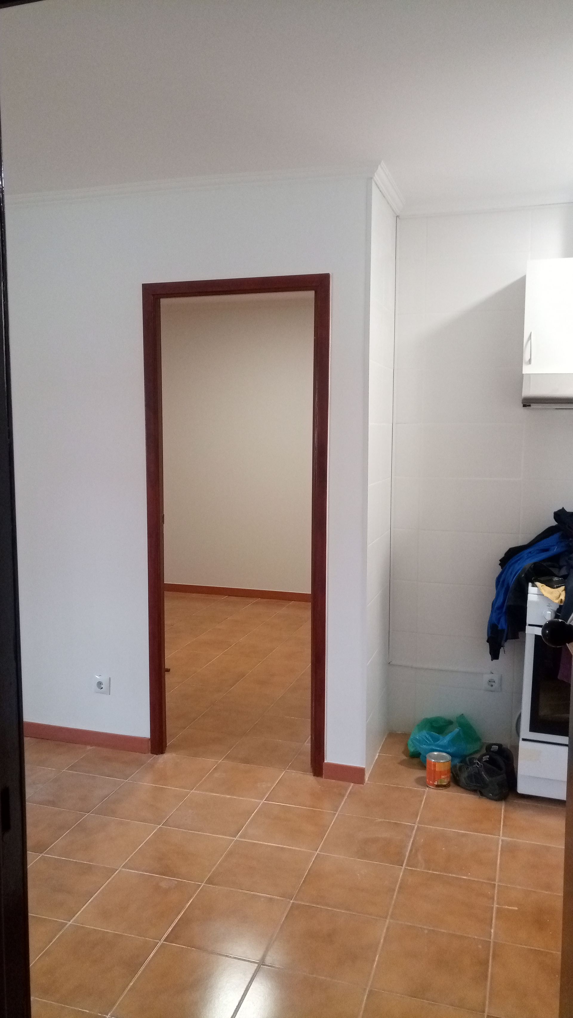 Porta de entrada para um cômodo com molduras marrons, paredes bege e piso de azulejo marrom. Eletrodomésticos da cozinha visíveis à direita.