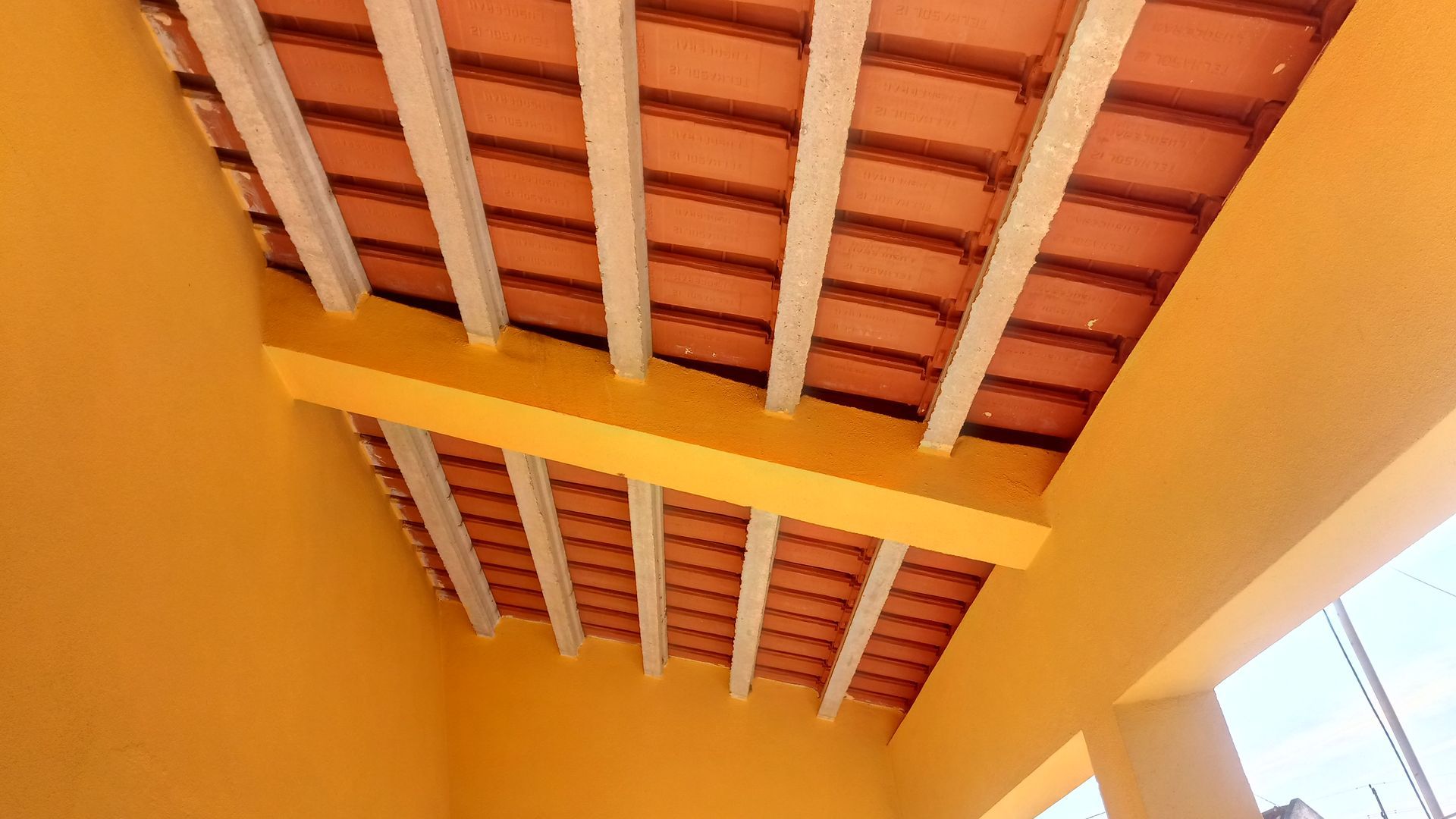 Teto amarelo com vigas brancas expostas e telhas de terracota.