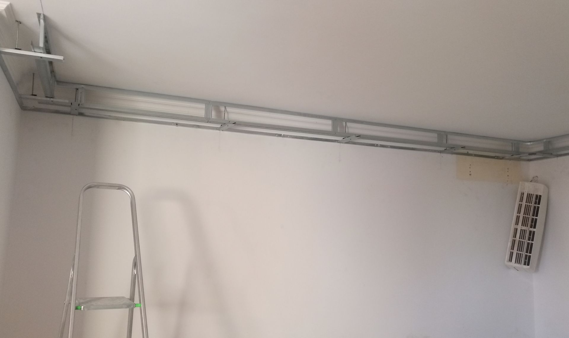 Canaleta metálica para cabos instalada ao longo de um canto do teto, com escada e ventilação na parede do cômodo.