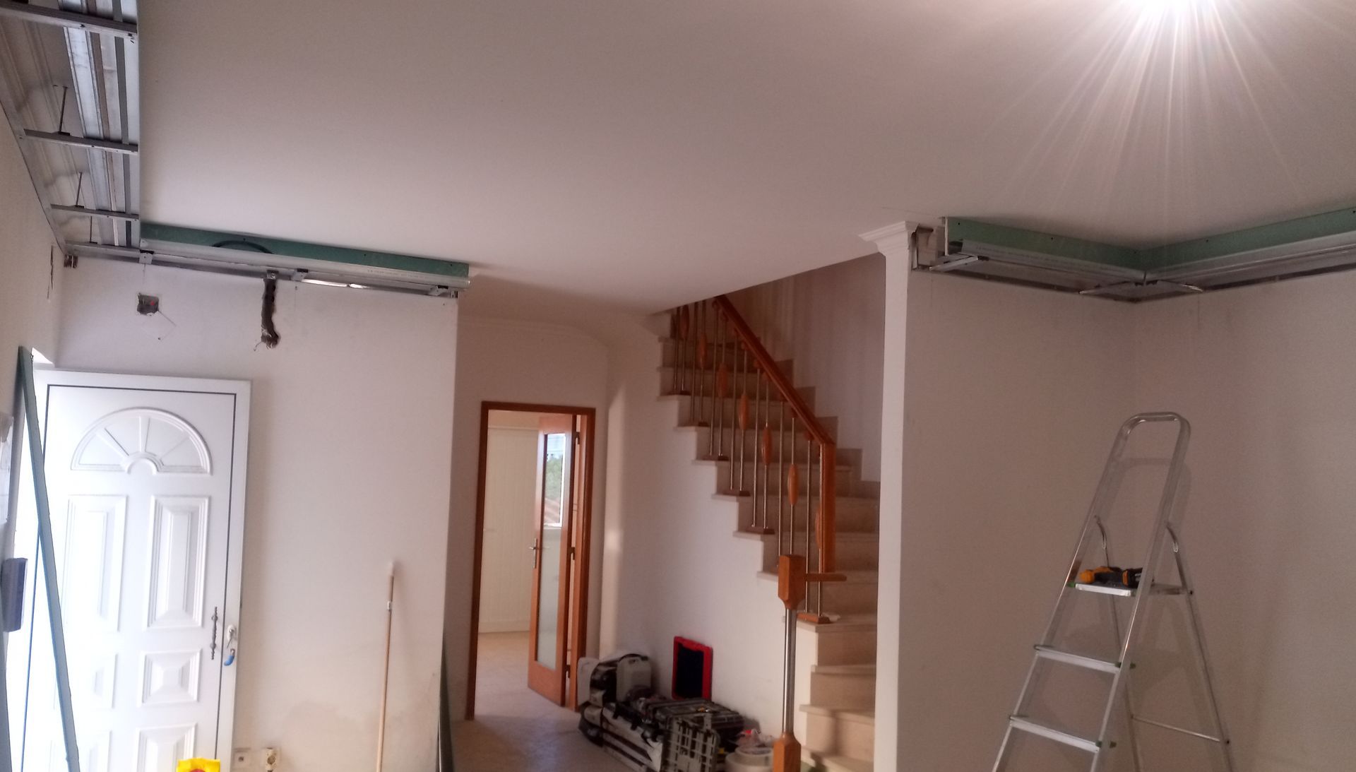 Vista interior de uma sala em construção com vigas de sustentação do teto expostas, escada e escada de mão.